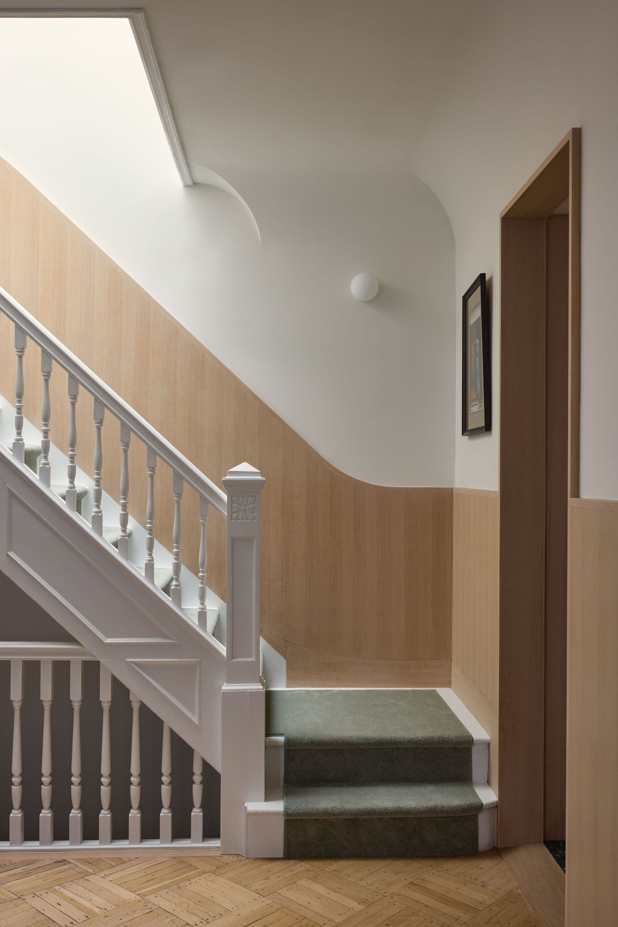Stair hall with white painted balusters, curved oak paneling and skylight above