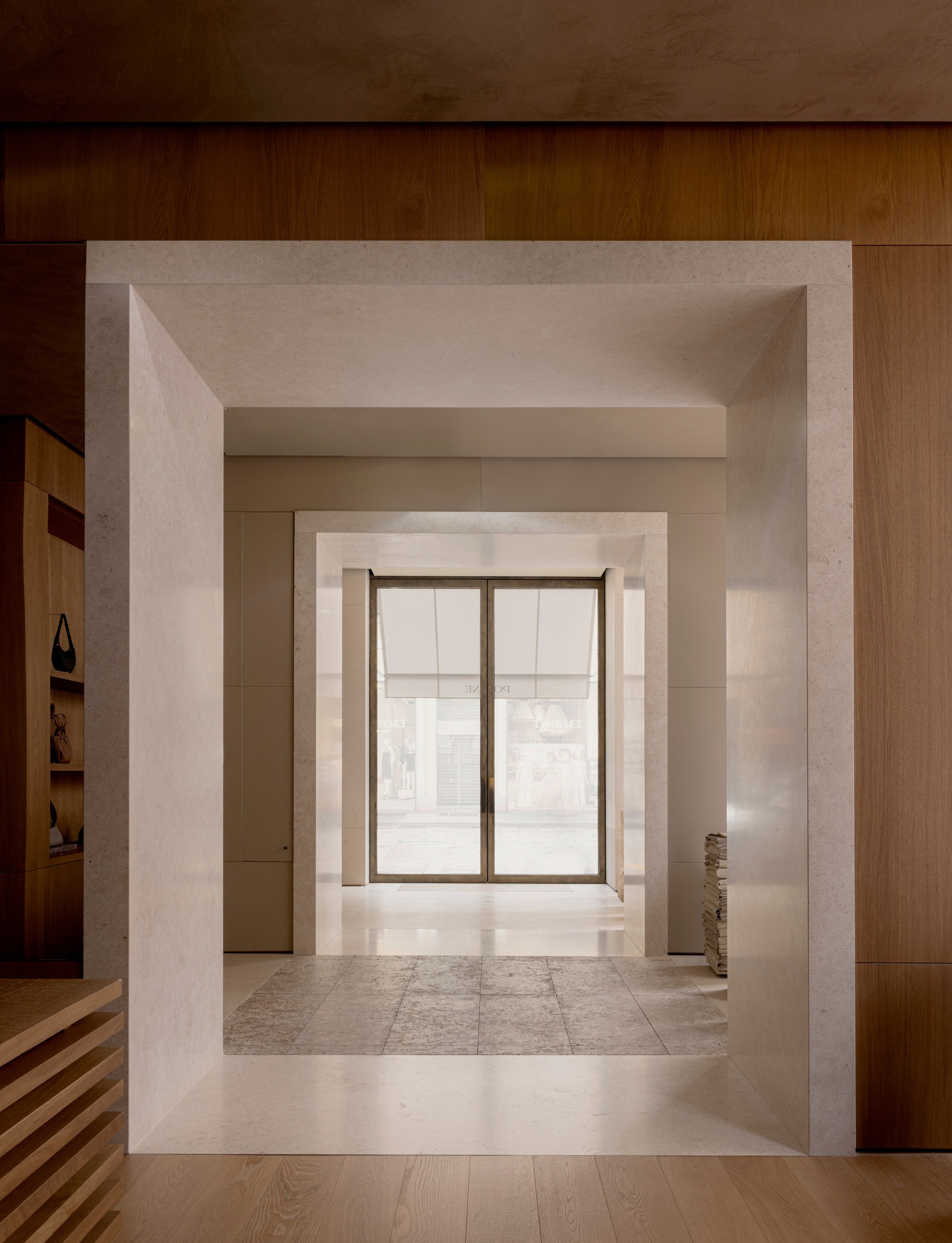 Enfilade of stone portals framing a glazed entrance at the far end under linear ceiling lighting