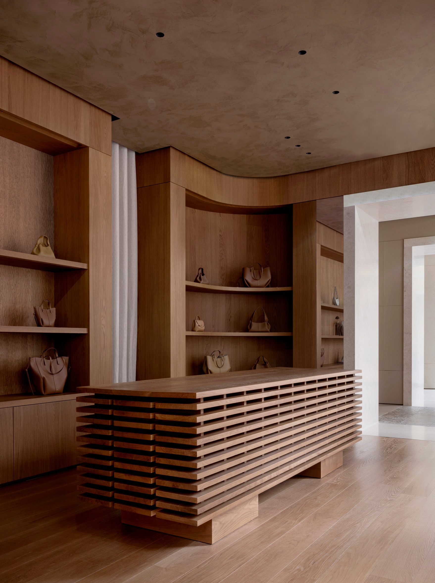 Timber display counter with horizontal slat base and curved shelving wall under a limestone ceiling