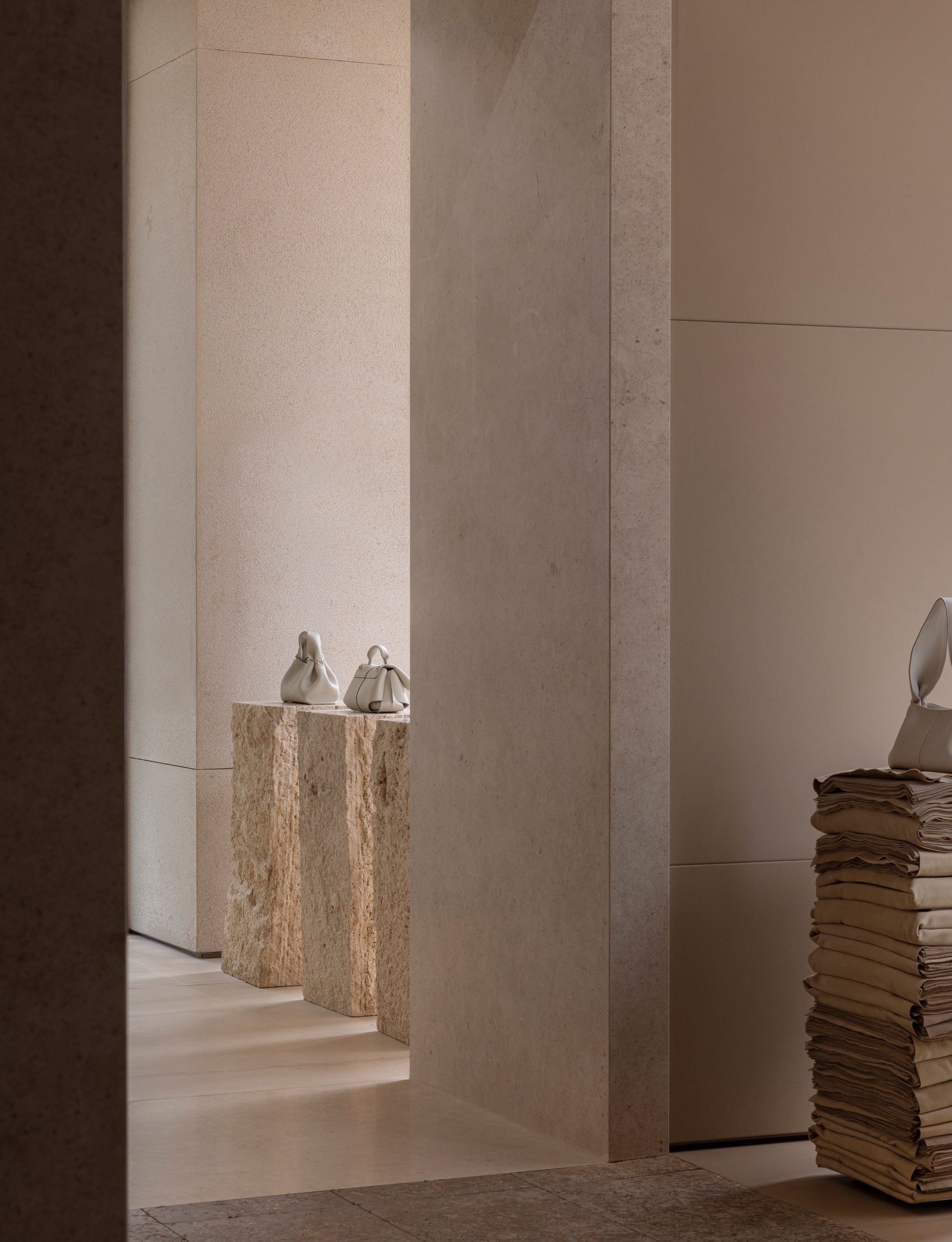 Doorway framed by concrete columns revealing travertine plinths with ceramic vessels in soft light