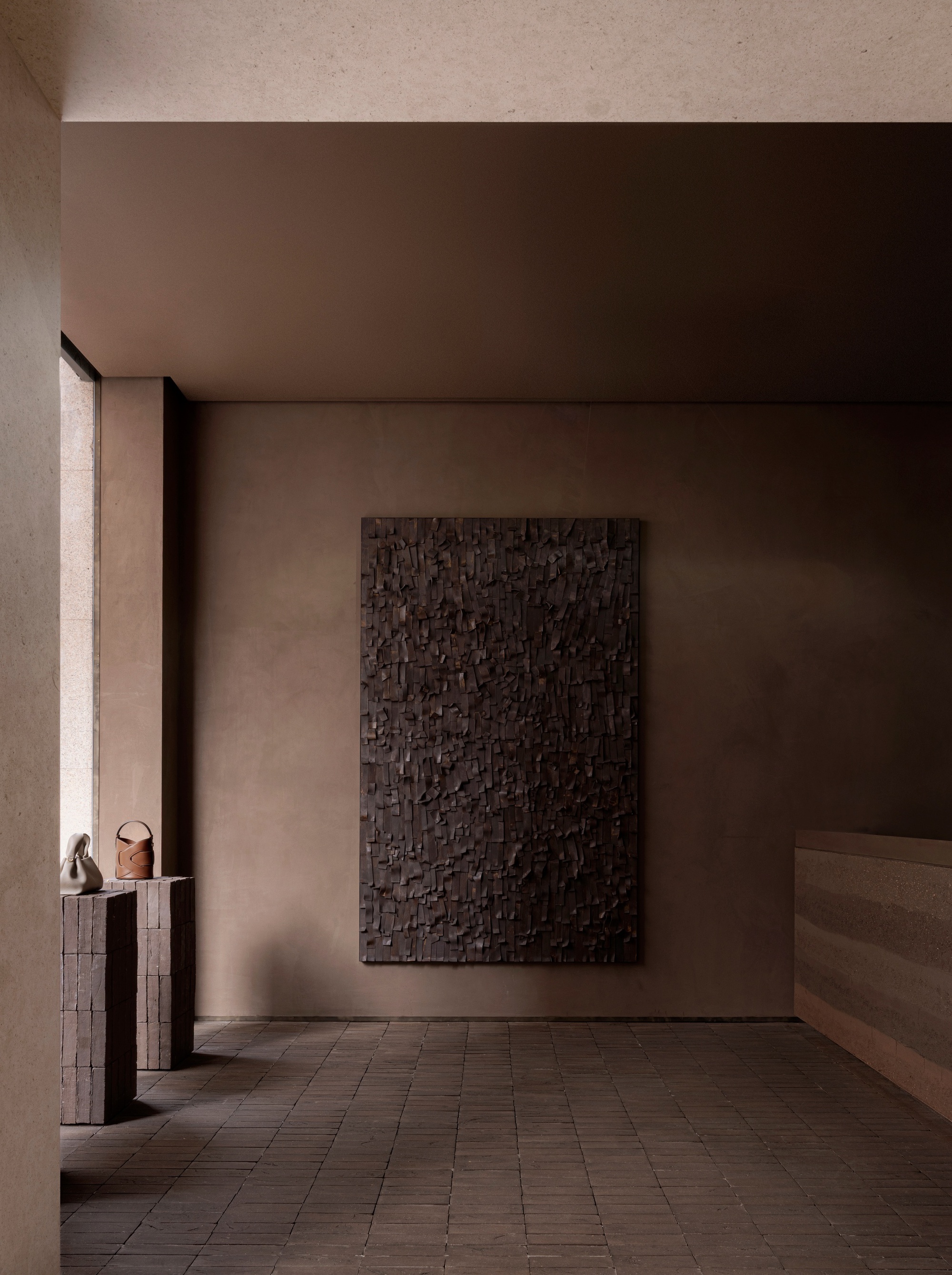 Gallery room with dark textured relief panel on taupe wall and brick tile flooring