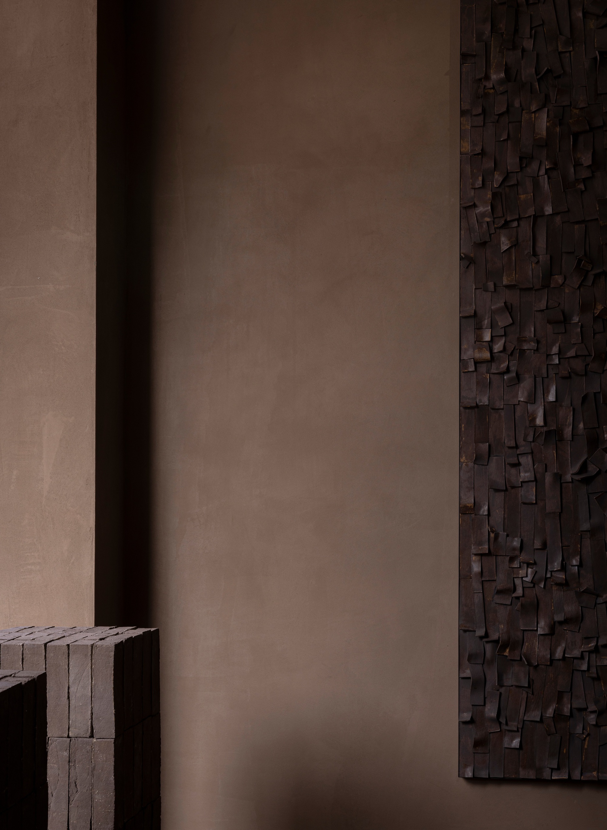 Close-up of dark wooden relief sculpture edge meeting smooth taupe plaster wall in shadow