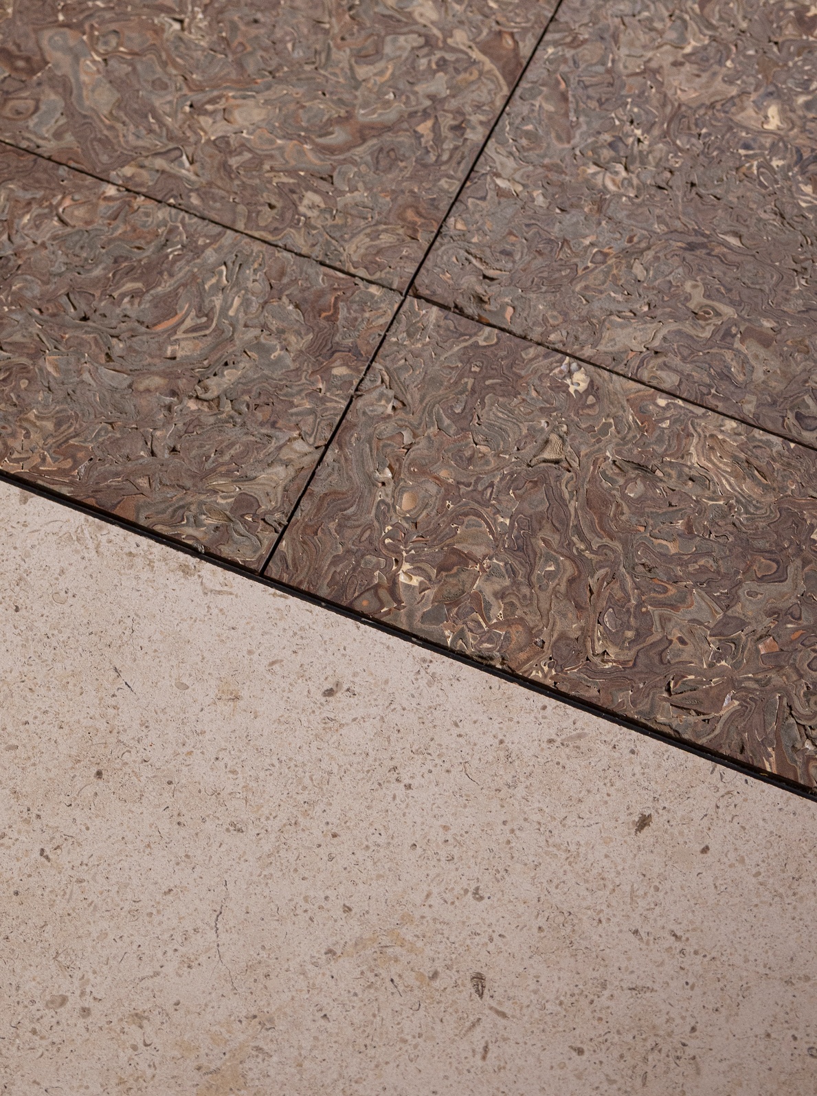 Close-up of marbled terrazzo flooring meeting pale stone tiles at a diagonal joint