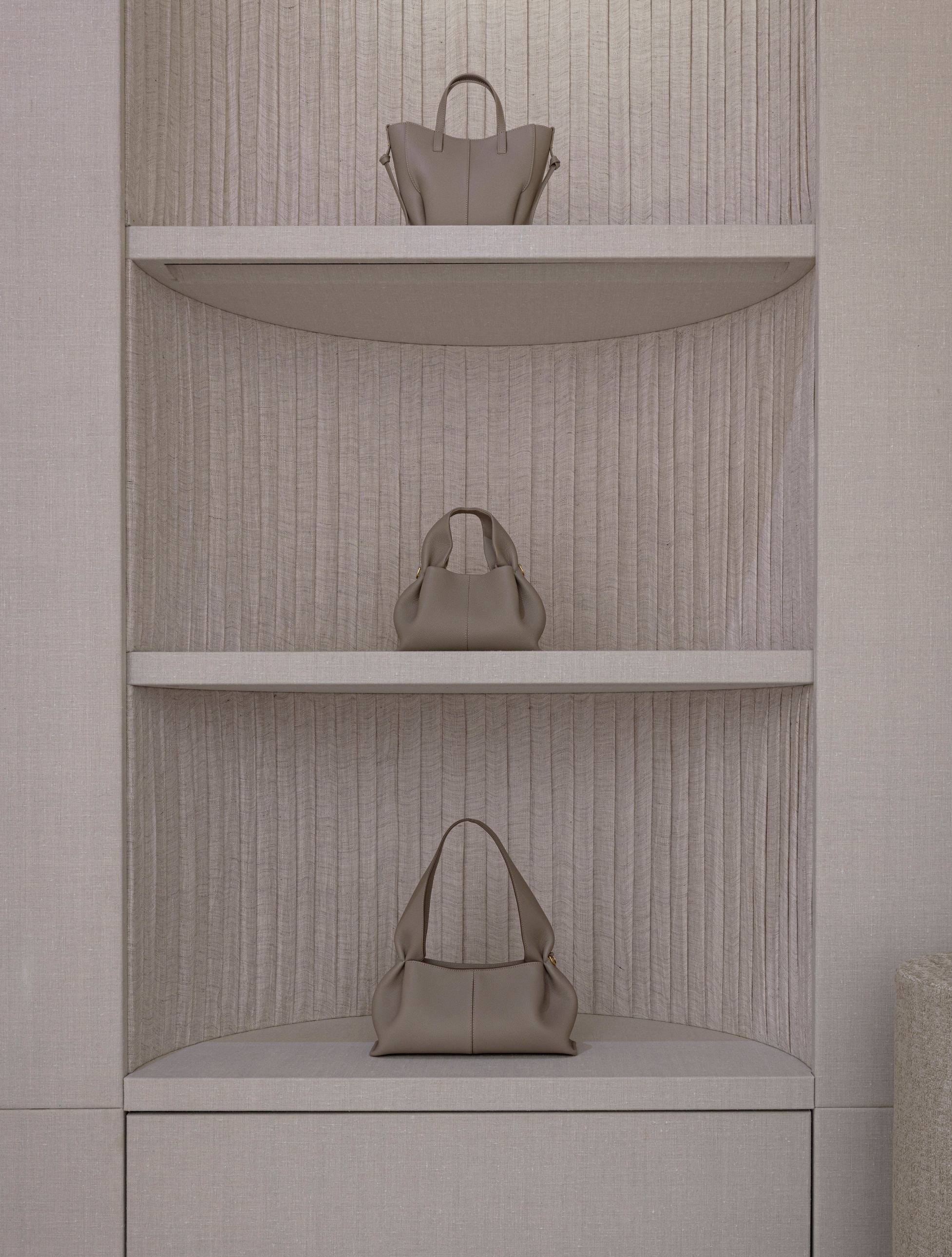 Curved corner shelving niche with fluted linen backing displaying three leather handbags
