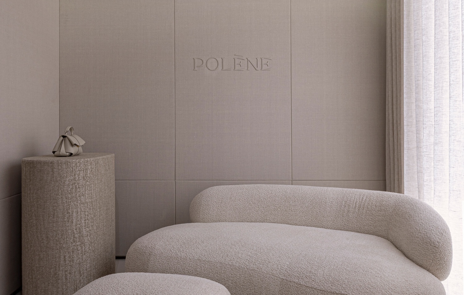 Textured wall panels with embossed lettering behind a rounded upholstered sofa and cylindrical side table