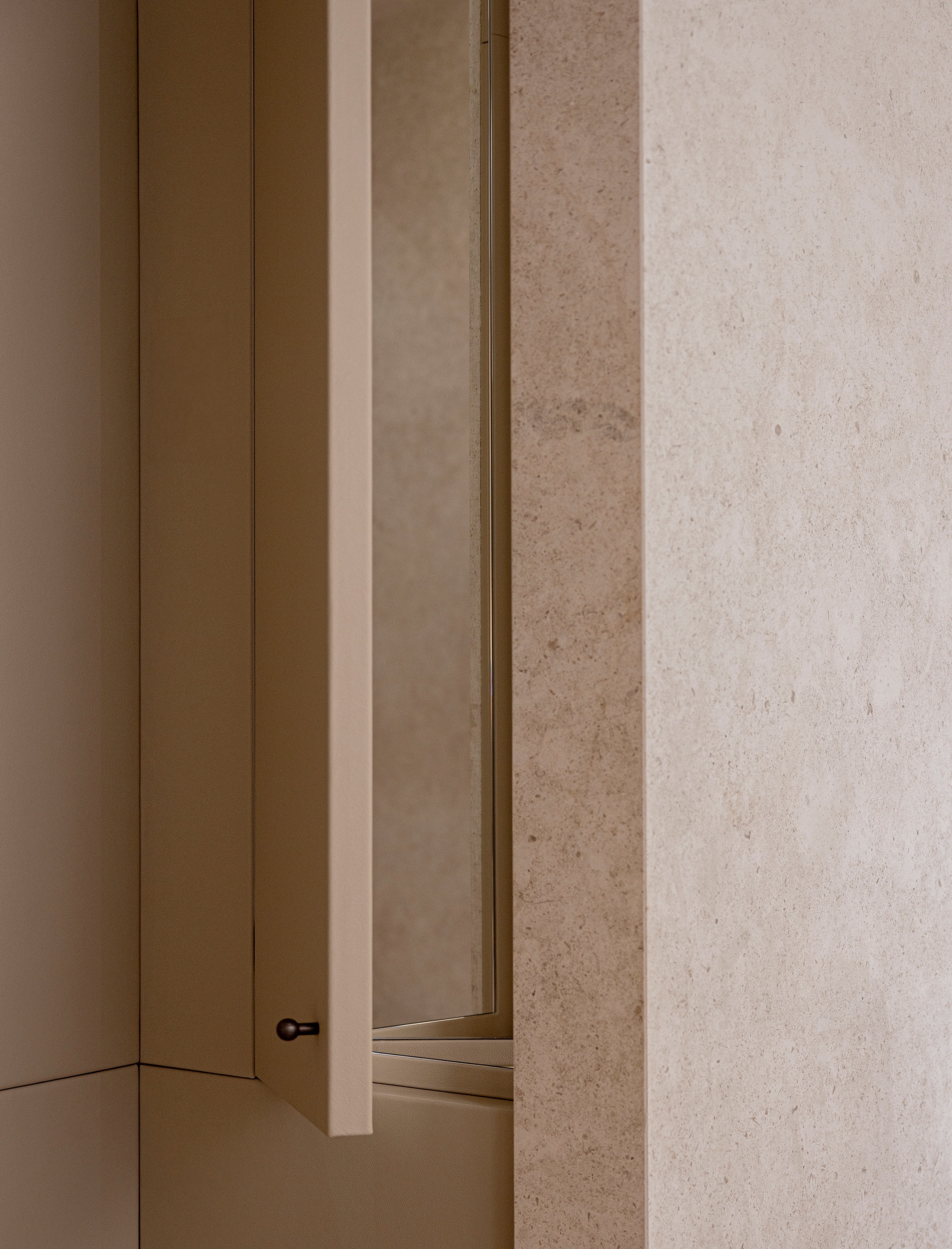 Detail of brass-edged door frame meeting textured limestone wall in warm interior light