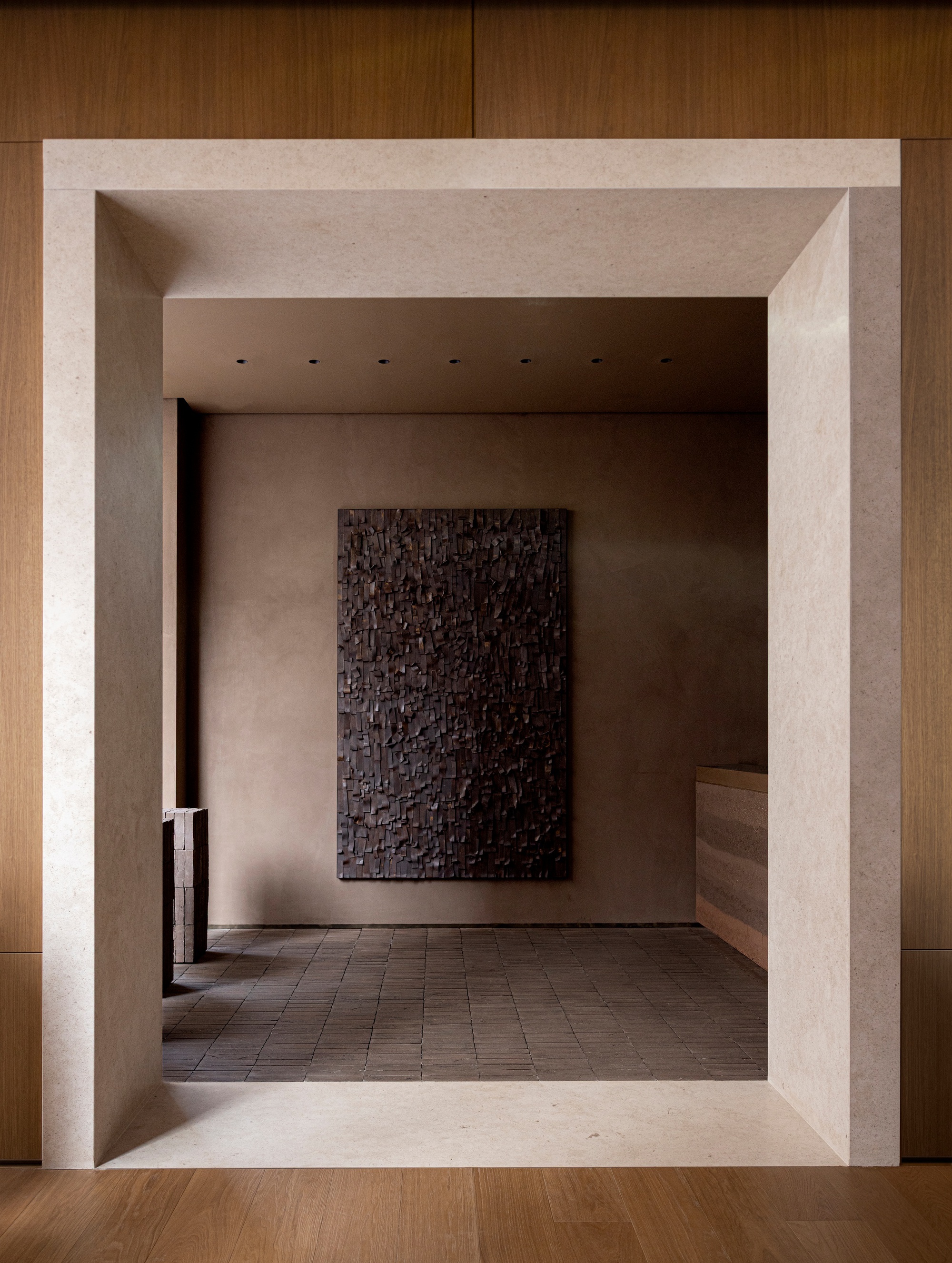 View through beveled stone threshold into a gallery space with textured artwork on rear wall