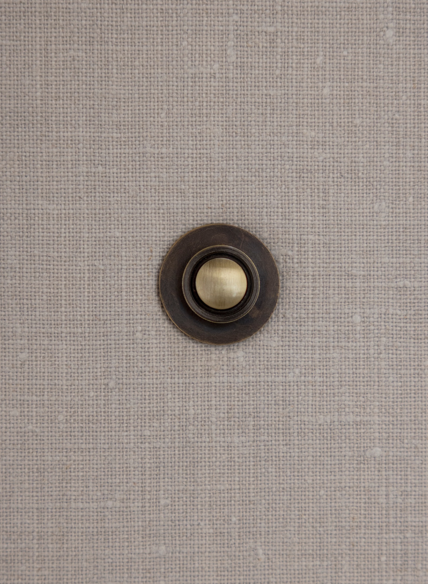 Close-up of bronze doorbell plate with brass button set into textured fabric wall covering