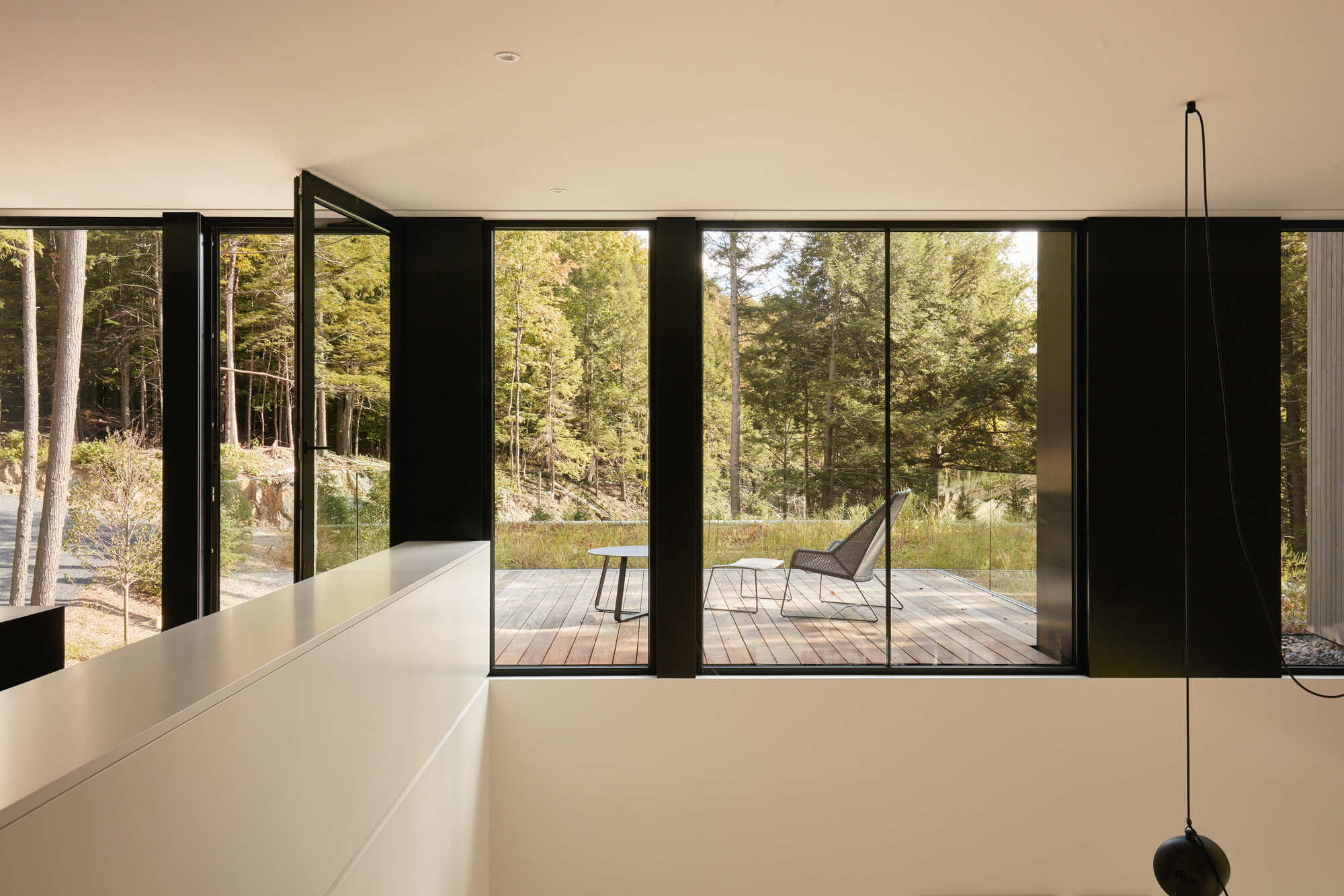 Black-framed sliding doors opening from upper level to a timber deck among the trees