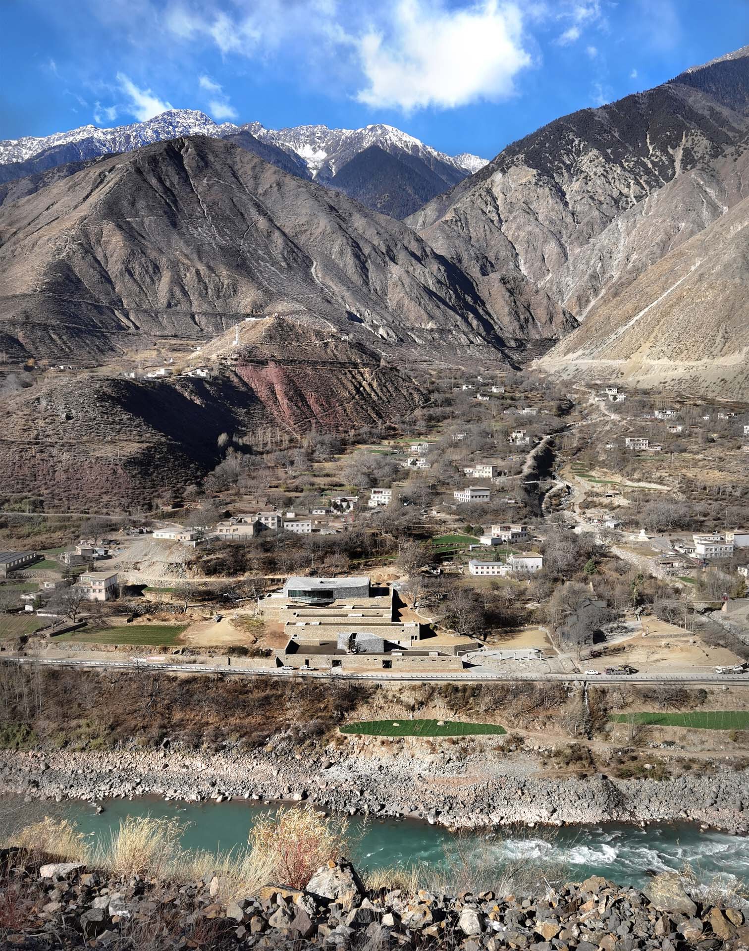 Riverside compound with horizontal stone terraces below snow-capped mountain ridges