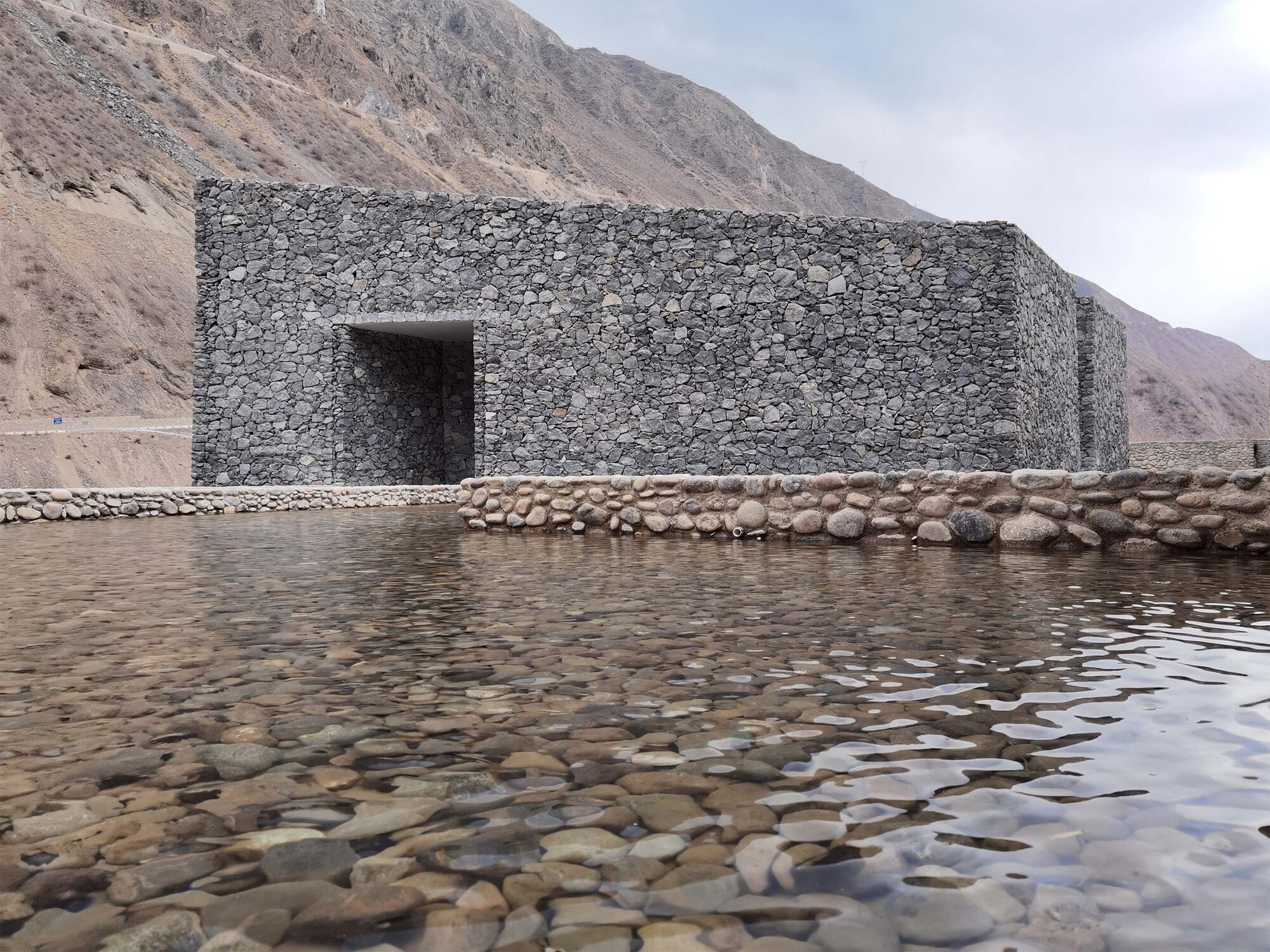 Stone gabion wall meeting a reflecting pool edged with river-rounded boulders