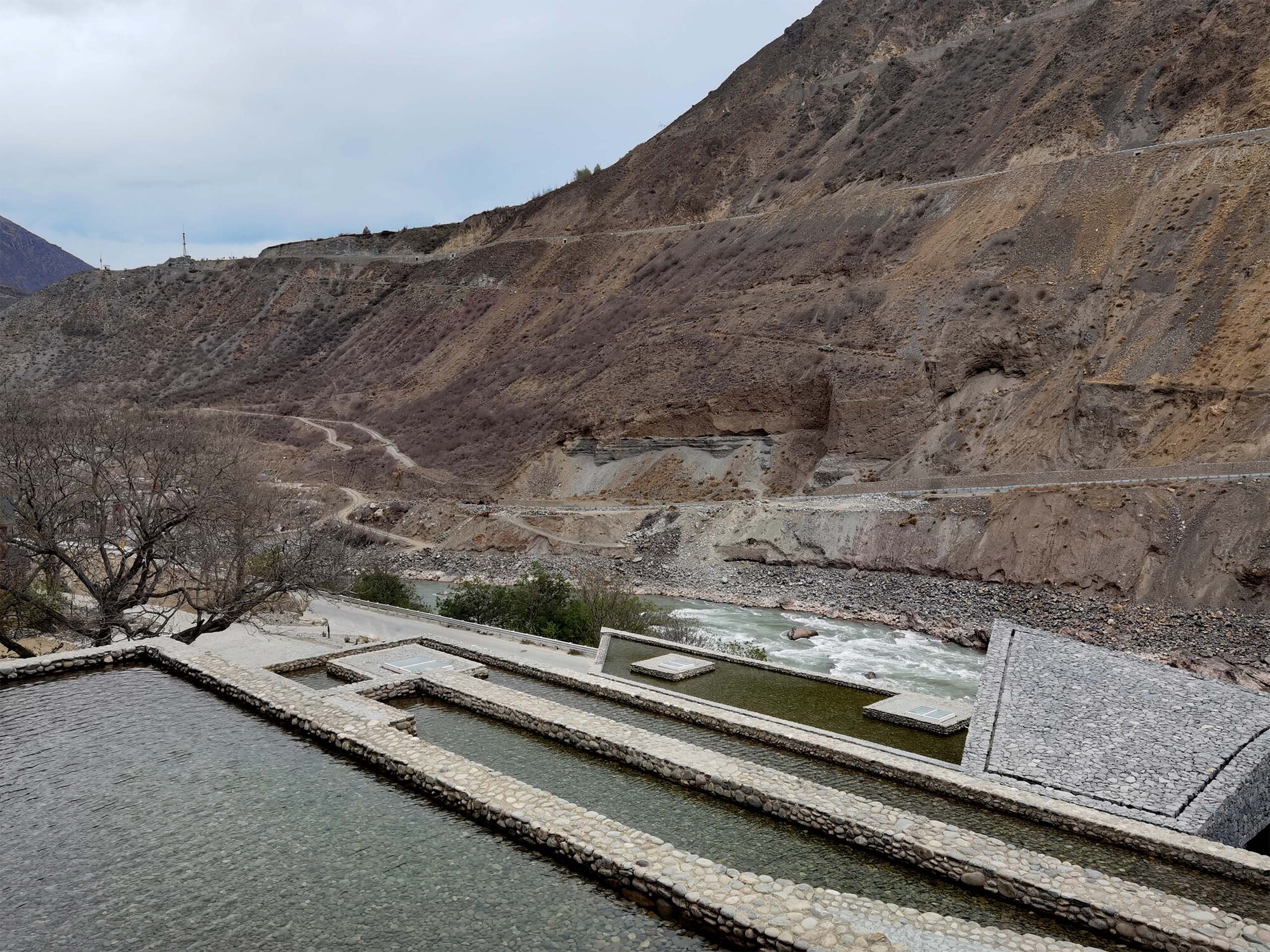 Water channels carved into stone terraces overlooking a riverbed in the barren mountain landscape