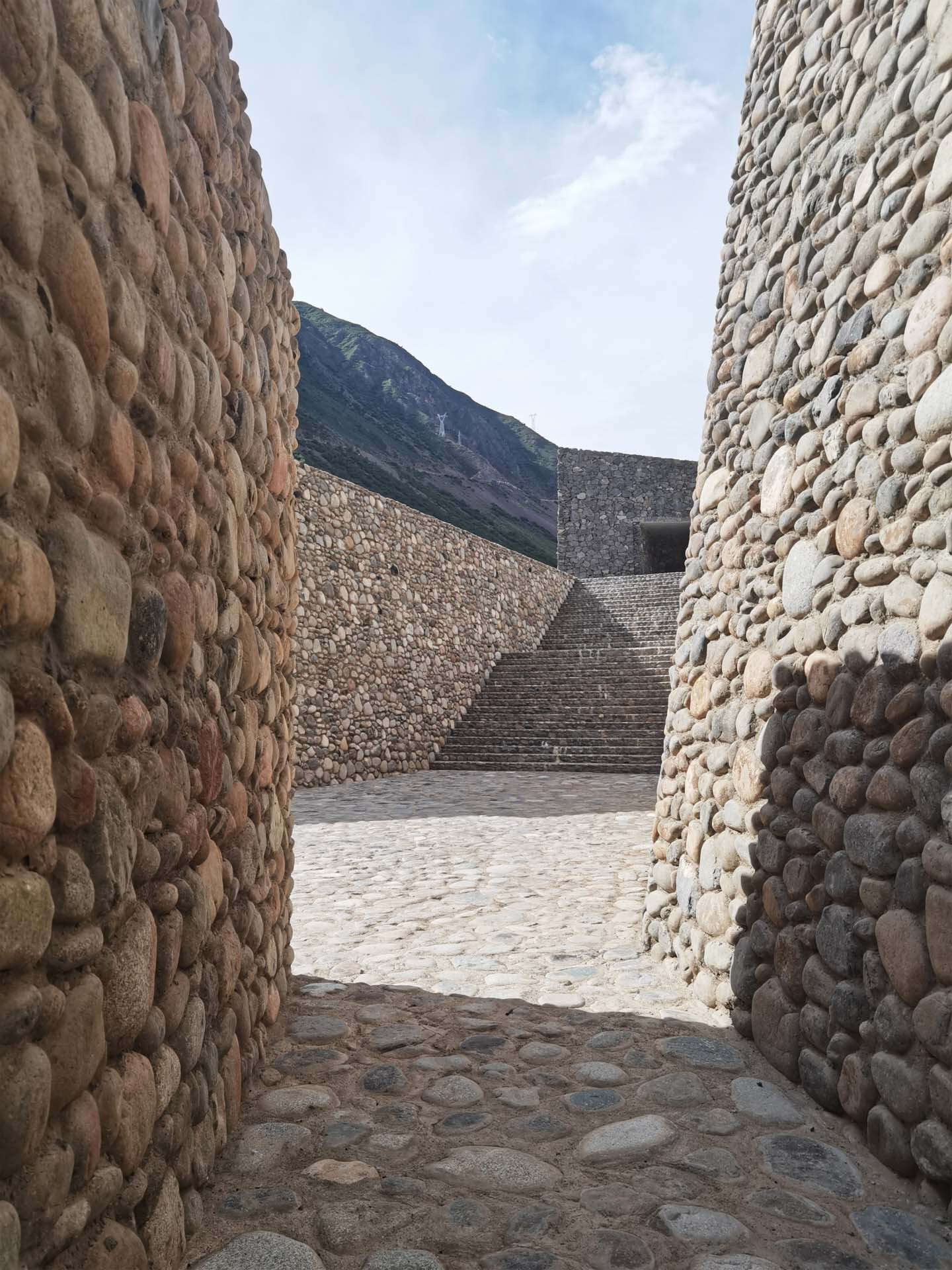View through stone passage toward ascending stairs and distant hillside in late afternoon light
