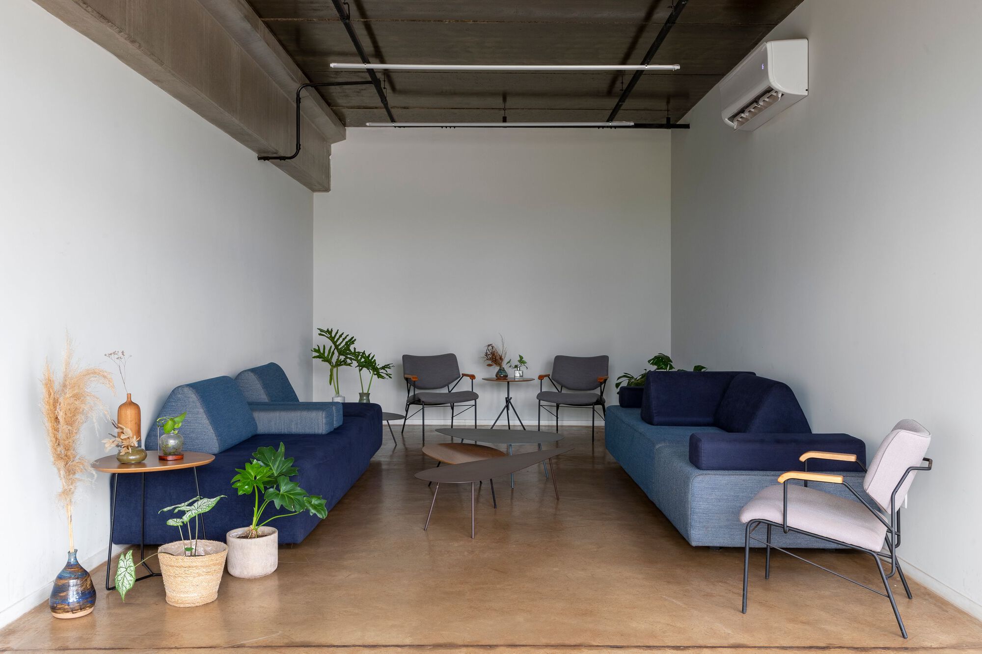 Lounge space with exposed concrete coffers and blue upholstered seating arranged around potted plants