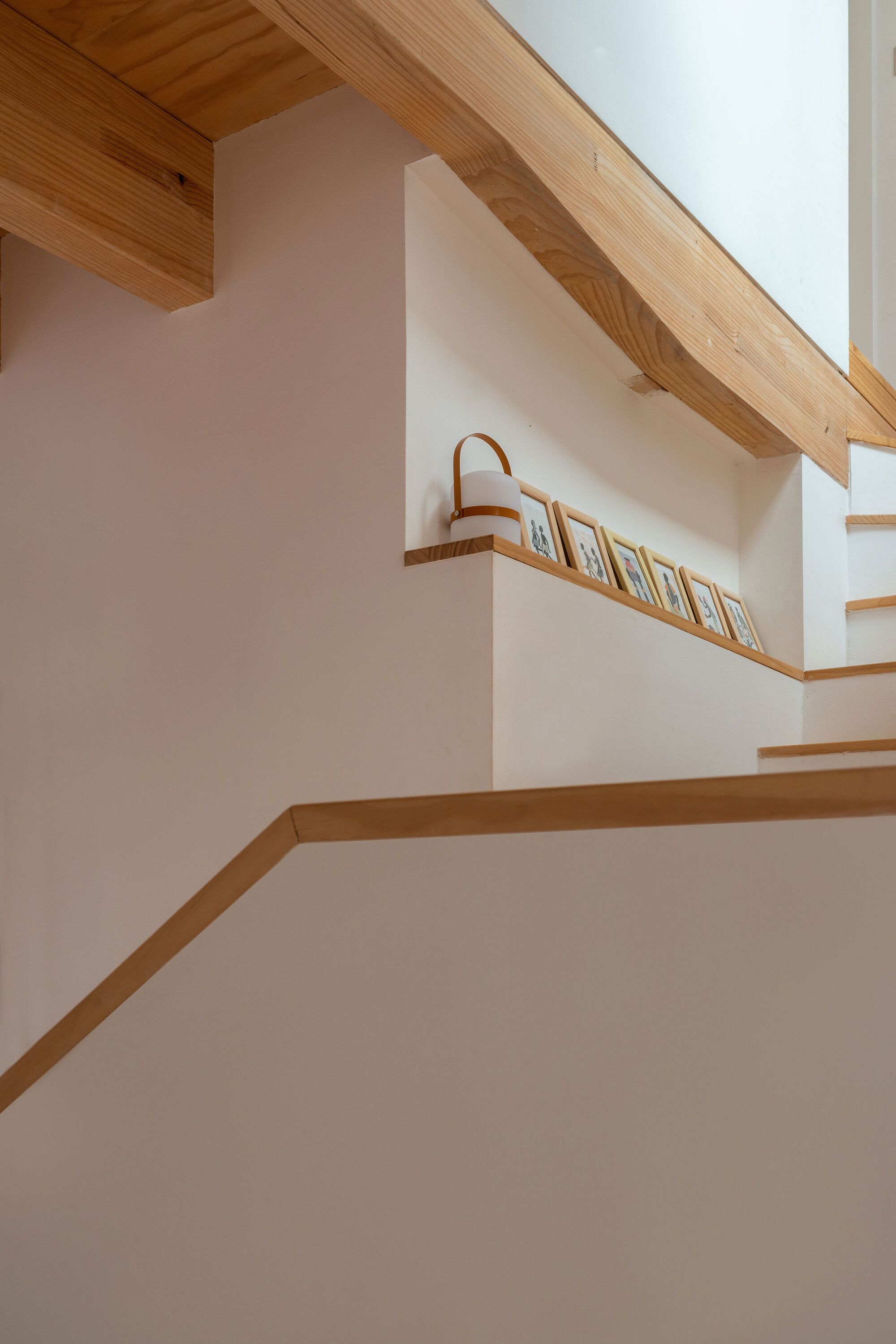 Interior staircase with timber treads and handrail ascending beneath exposed timber ceiling joists and white plaster walls