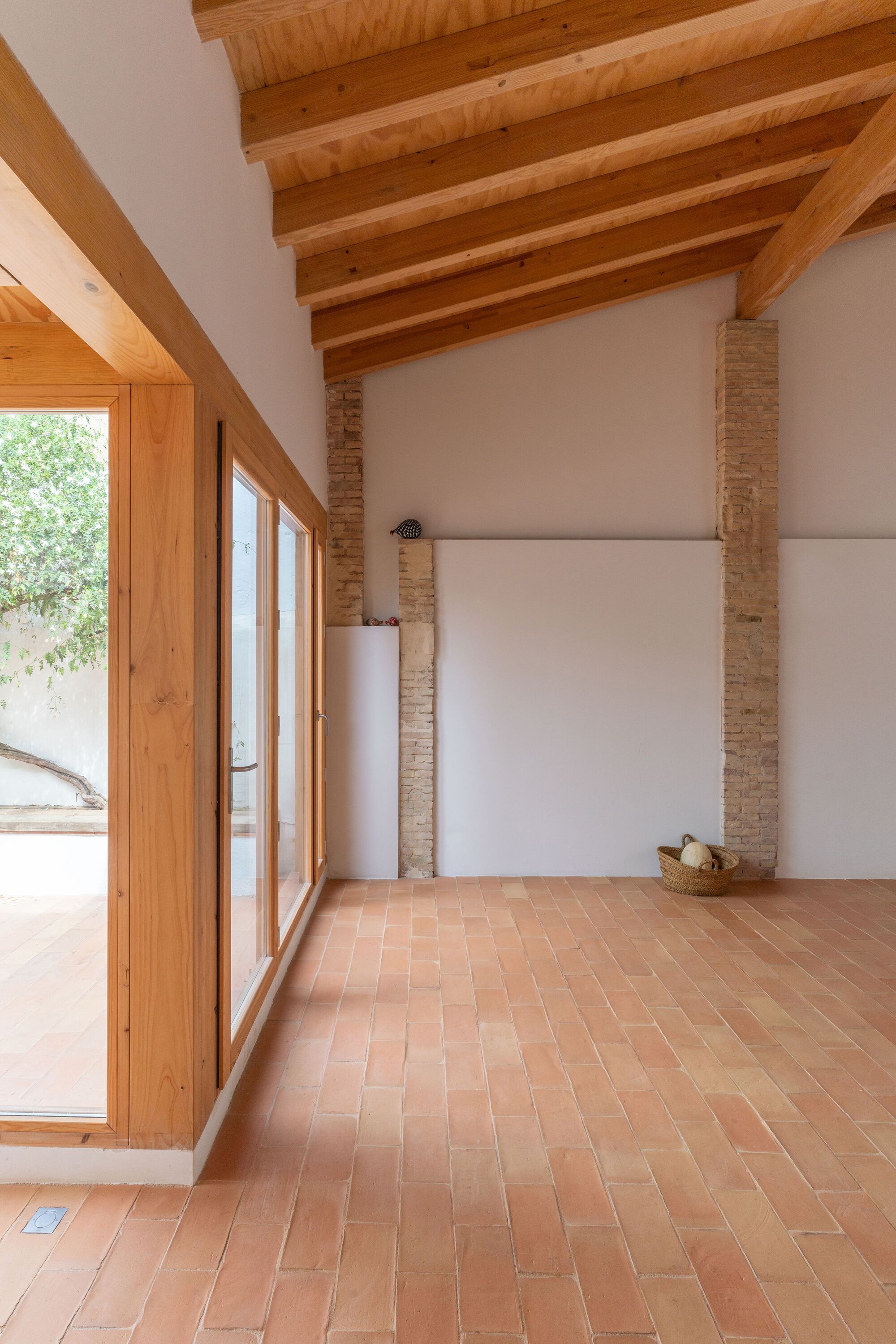 Corner of room with terracotta tile floor showing timber framed window and exposed brick column