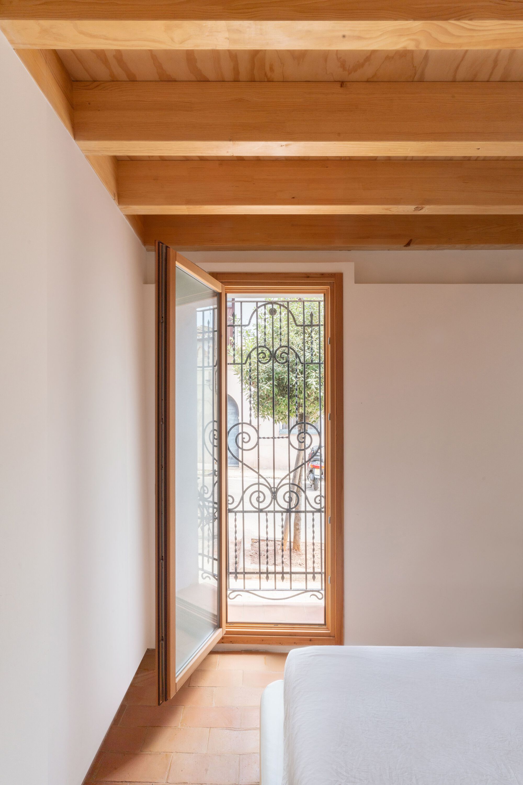 Bedroom corner with timber-framed door opening to exterior with decorative ironwork grille beyond exposed ceiling beams