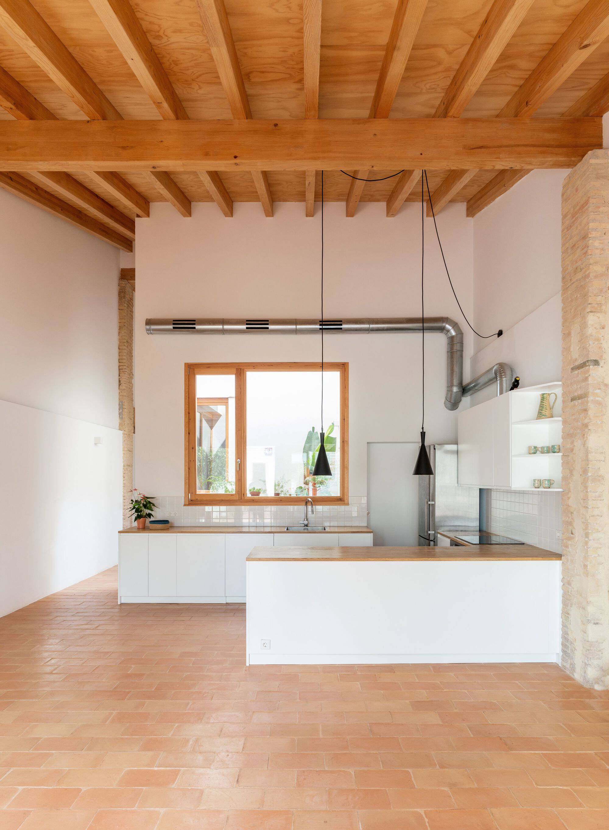 Open kitchen with white island, exposed timber ceiling beams, terracotta floor tiles and pendant lights