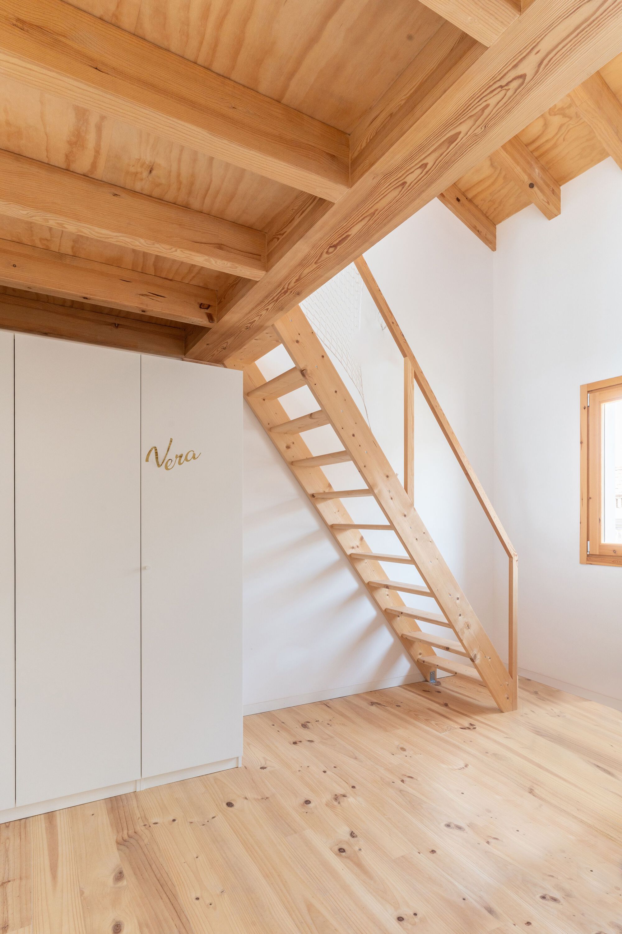 Timber ladder stair with open treads against white wall beneath exposed beam ceiling structure