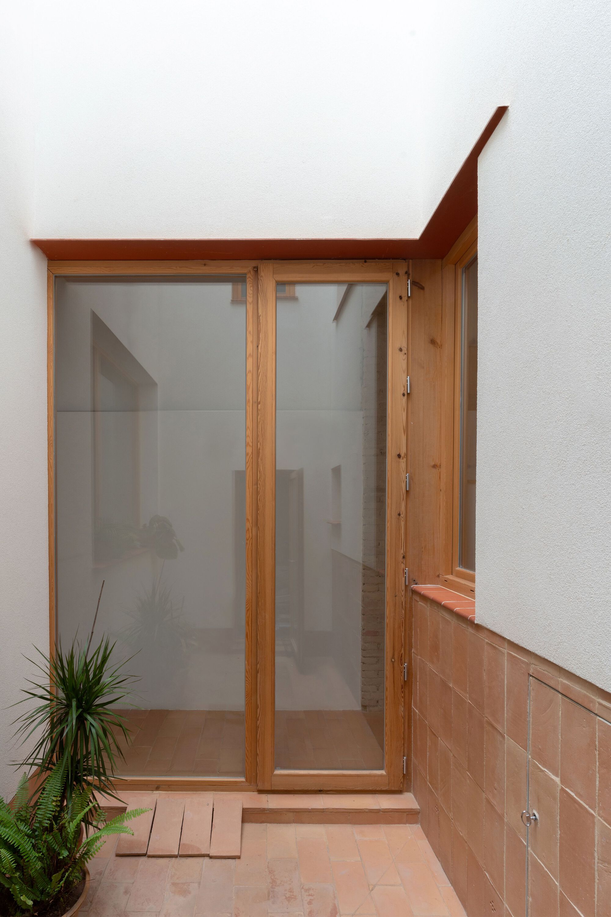 Small courtyard with timber-framed glass doors, terracotta paving and single potted plant in corner