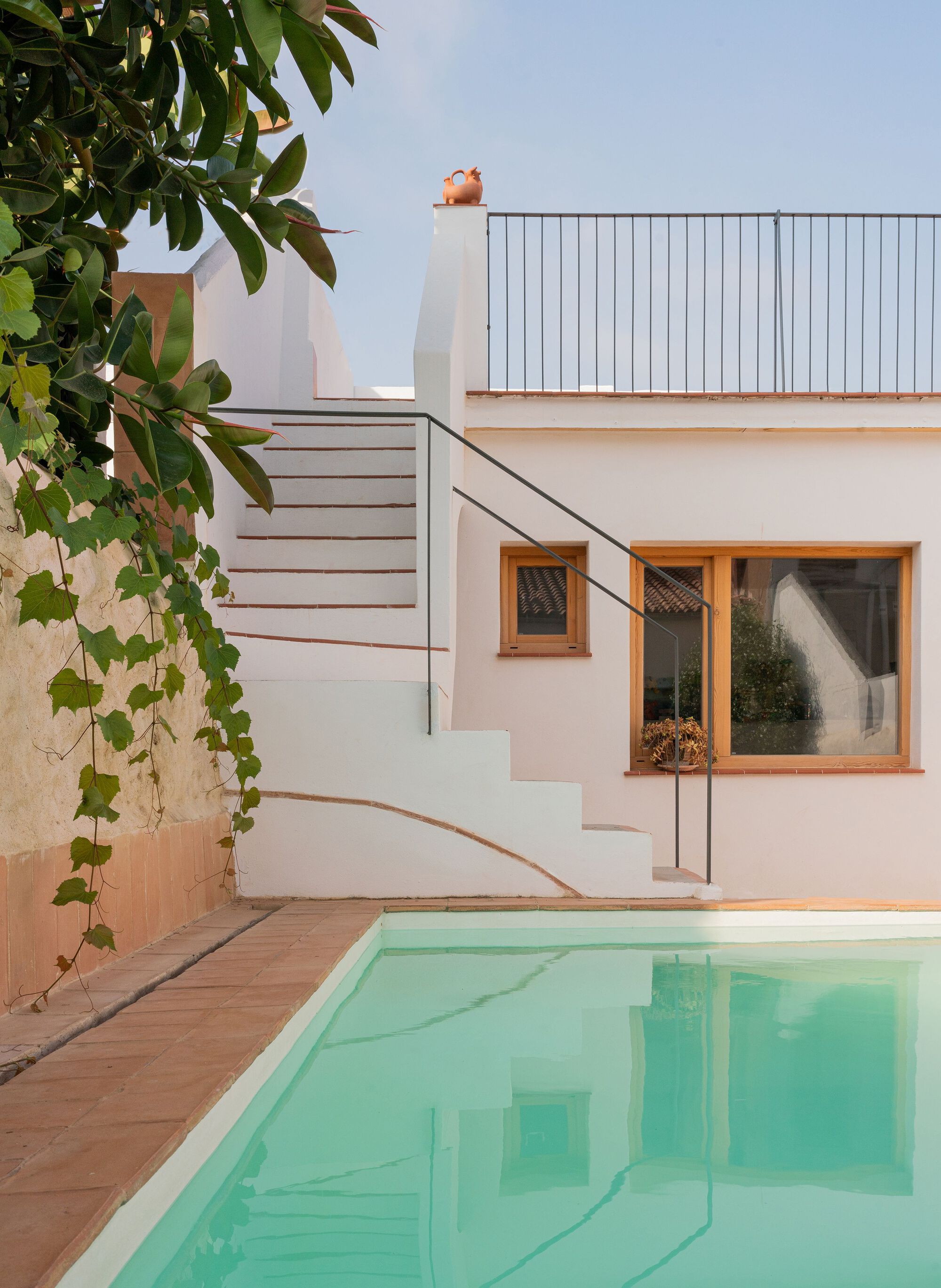 Courtyard pool with white exterior stair leading to rooftop terrace at dusk beside climbing vines