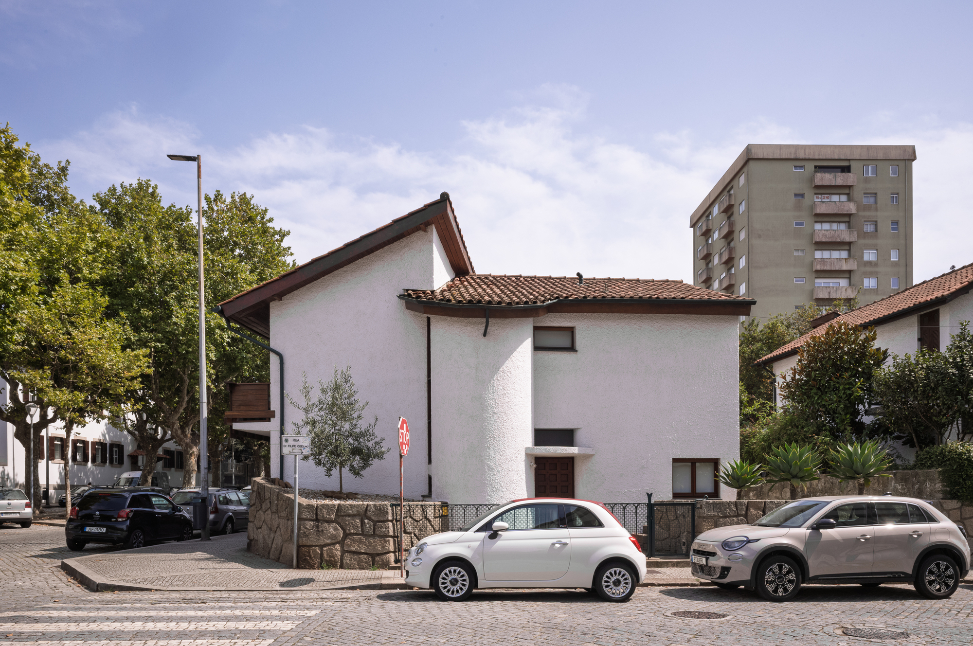 Street view of the white stucco house with terracotta tile roof between parked cars