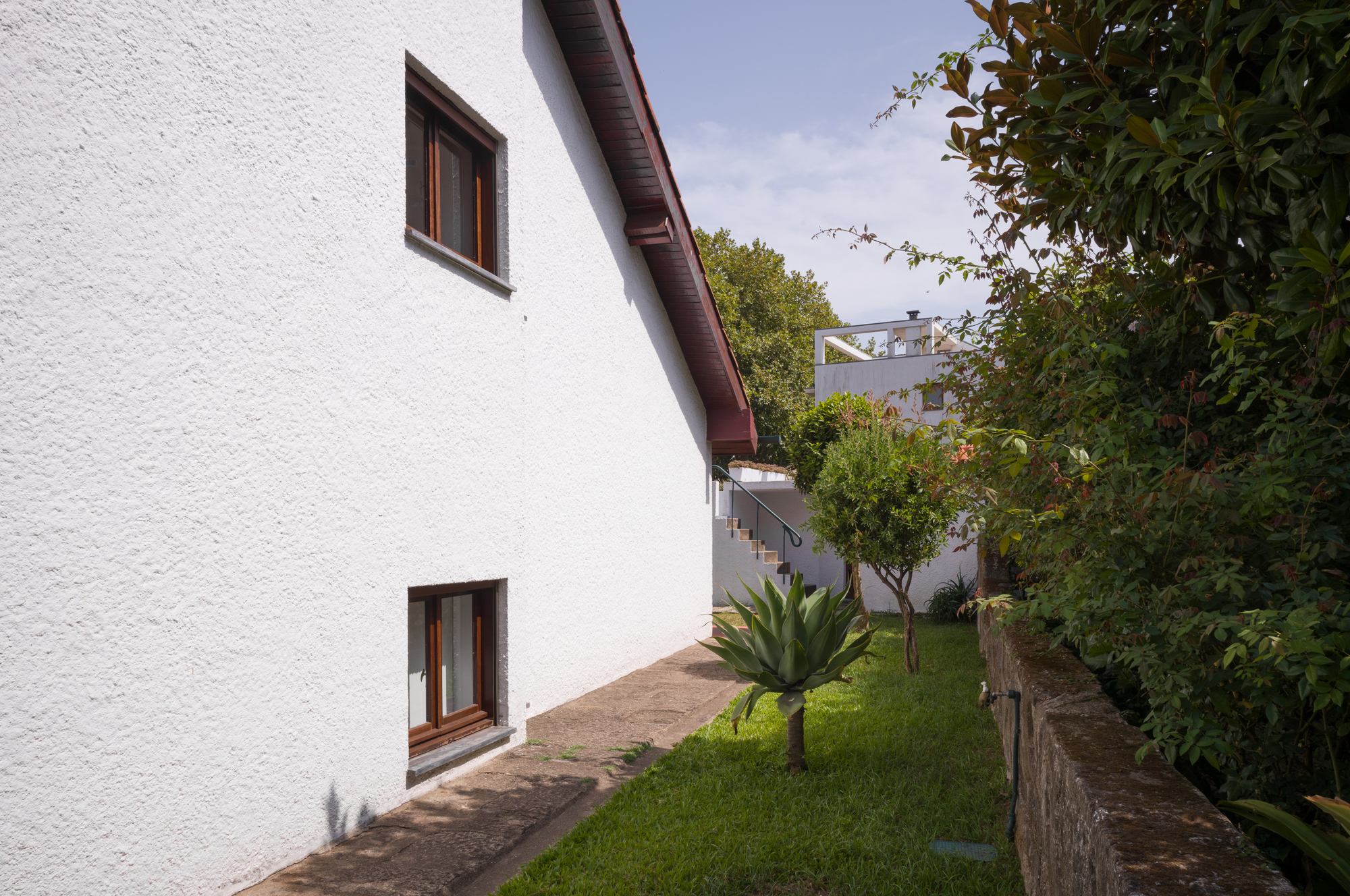 White stucco facade with timber-framed windows alongside a sloped garden path with an agave plant