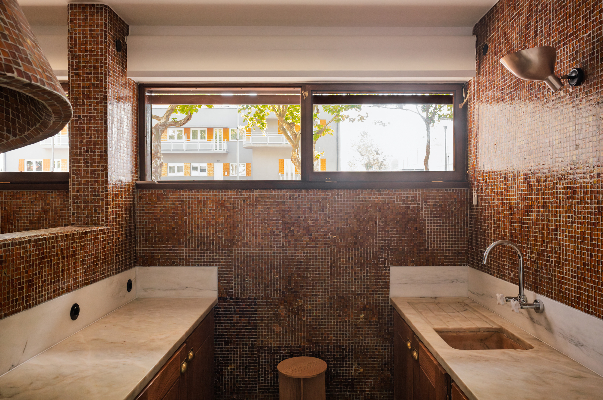 Kitchen with bronze mosaic tile surfaces and ribbon windows overlooking trees outside