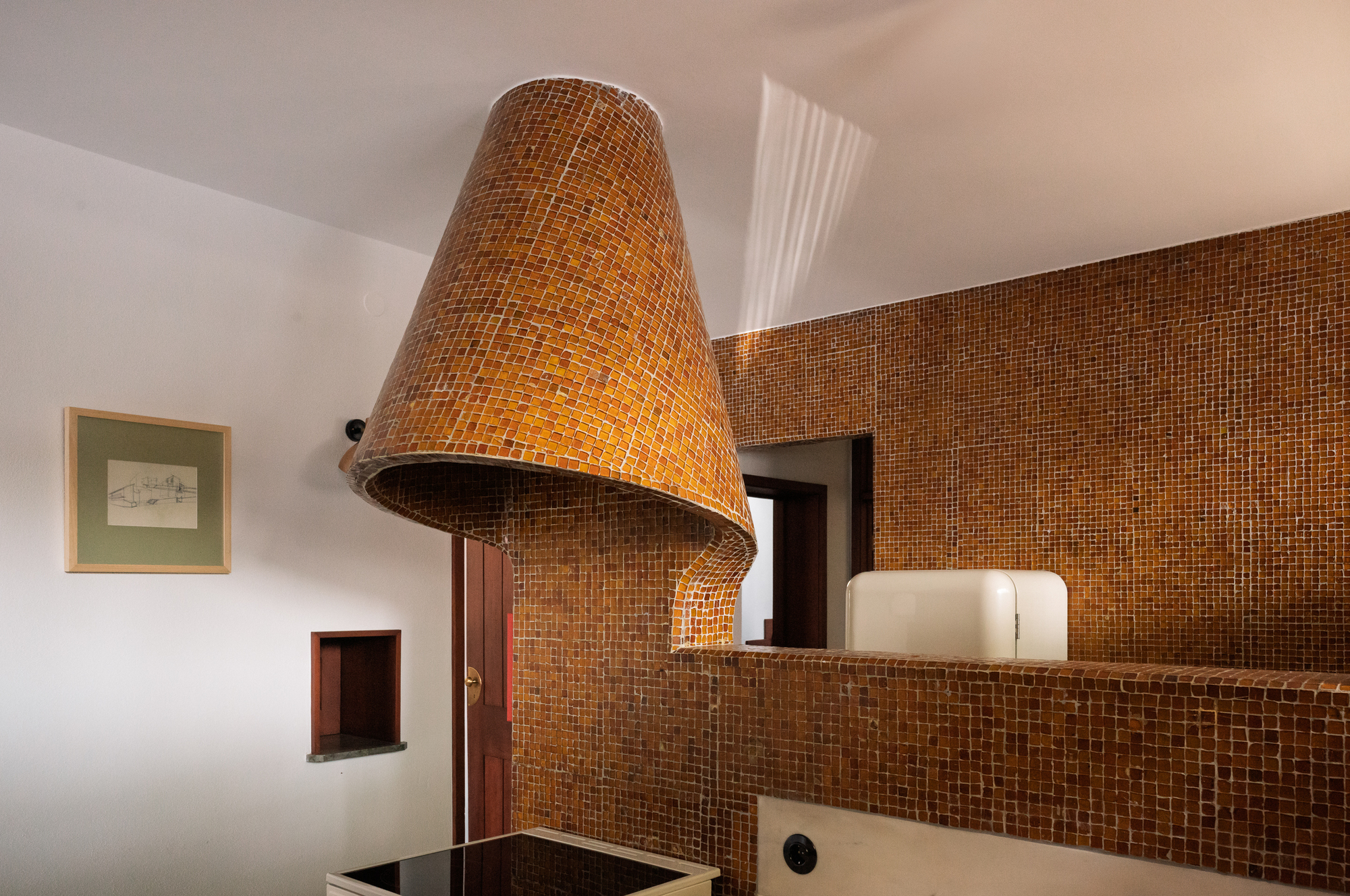 Conical bronze mosaic tile range hood above the cooktop with skylight overhead