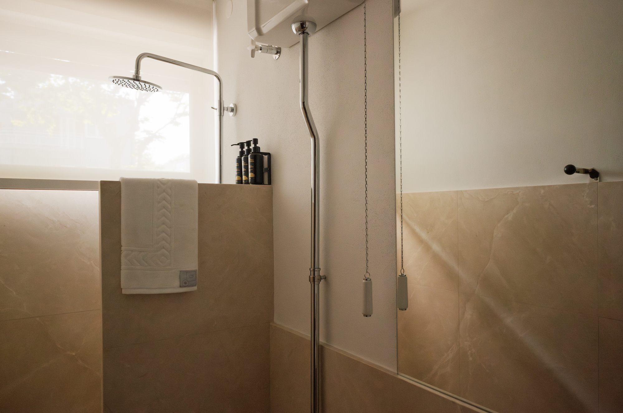 Shower enclosure with beige stone panels and exposed plumbing with chain-pull controls