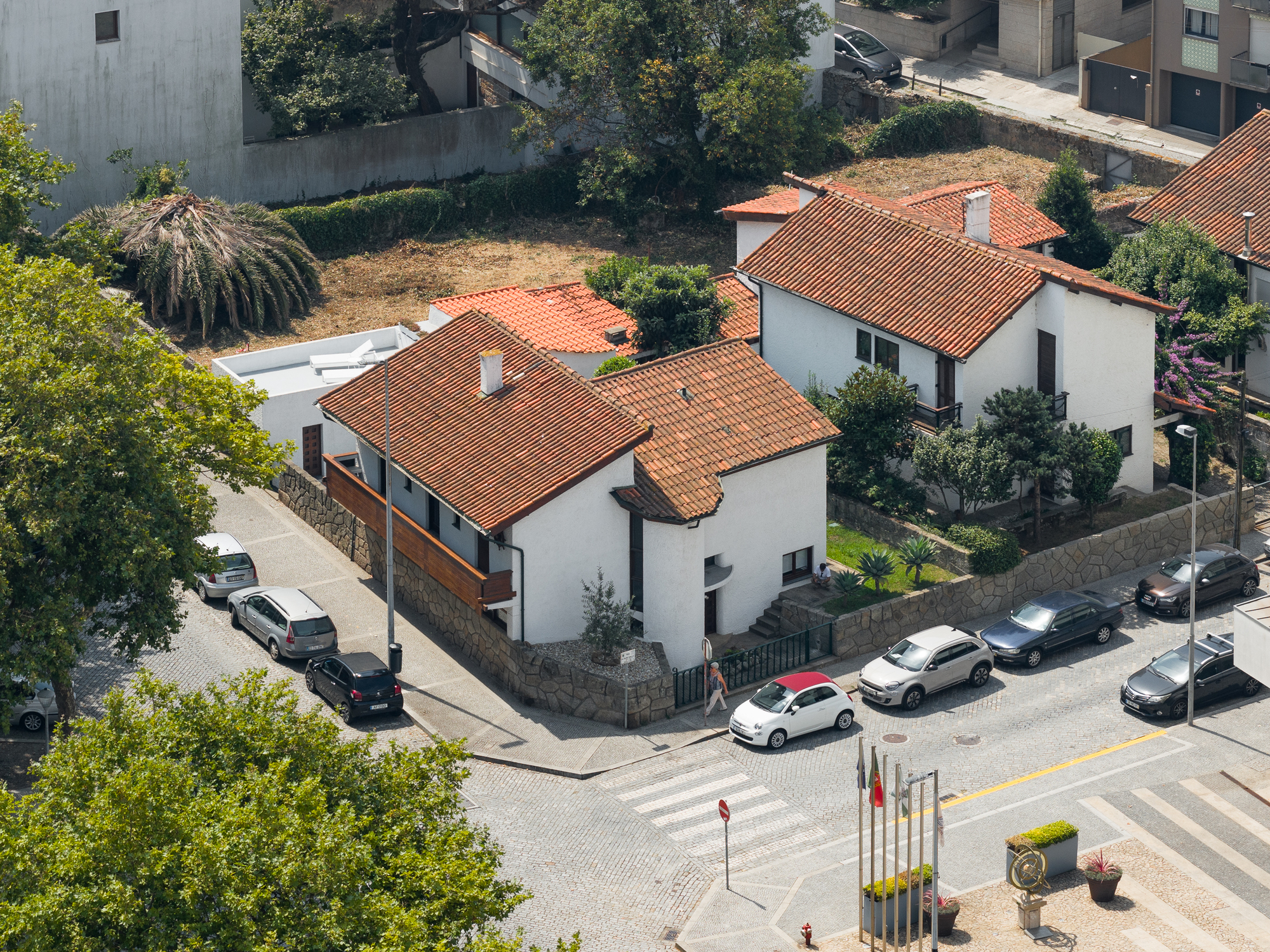 Aerial view of white stucco volumes with terracotta tile roofs at a street intersection