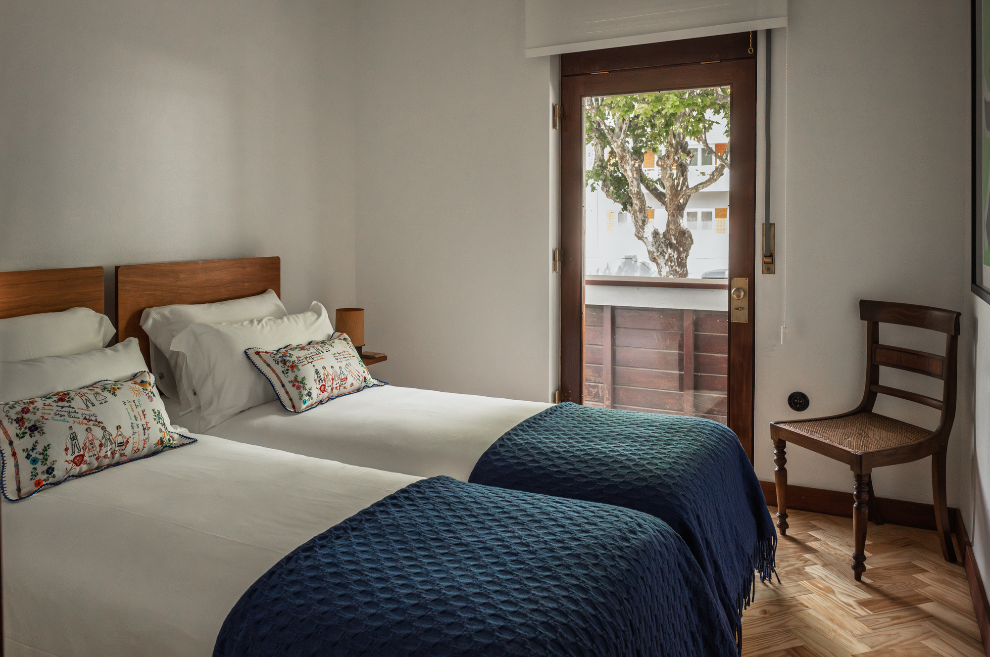 Twin beds with herringbone flooring and window framing a gnarled tree outside
