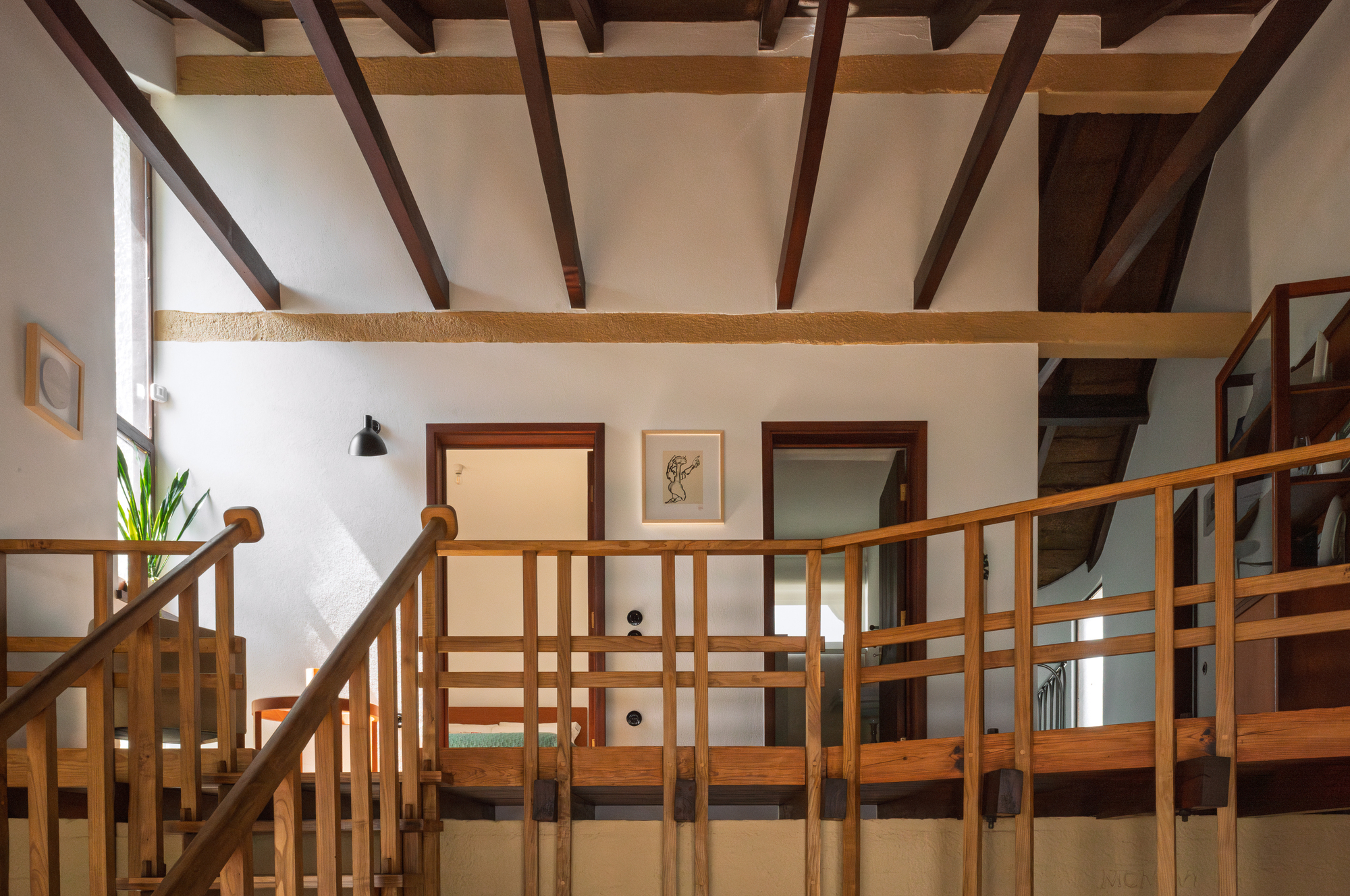 Timber railings around an upper level balcony with exposed ceiling beams and white plaster walls
