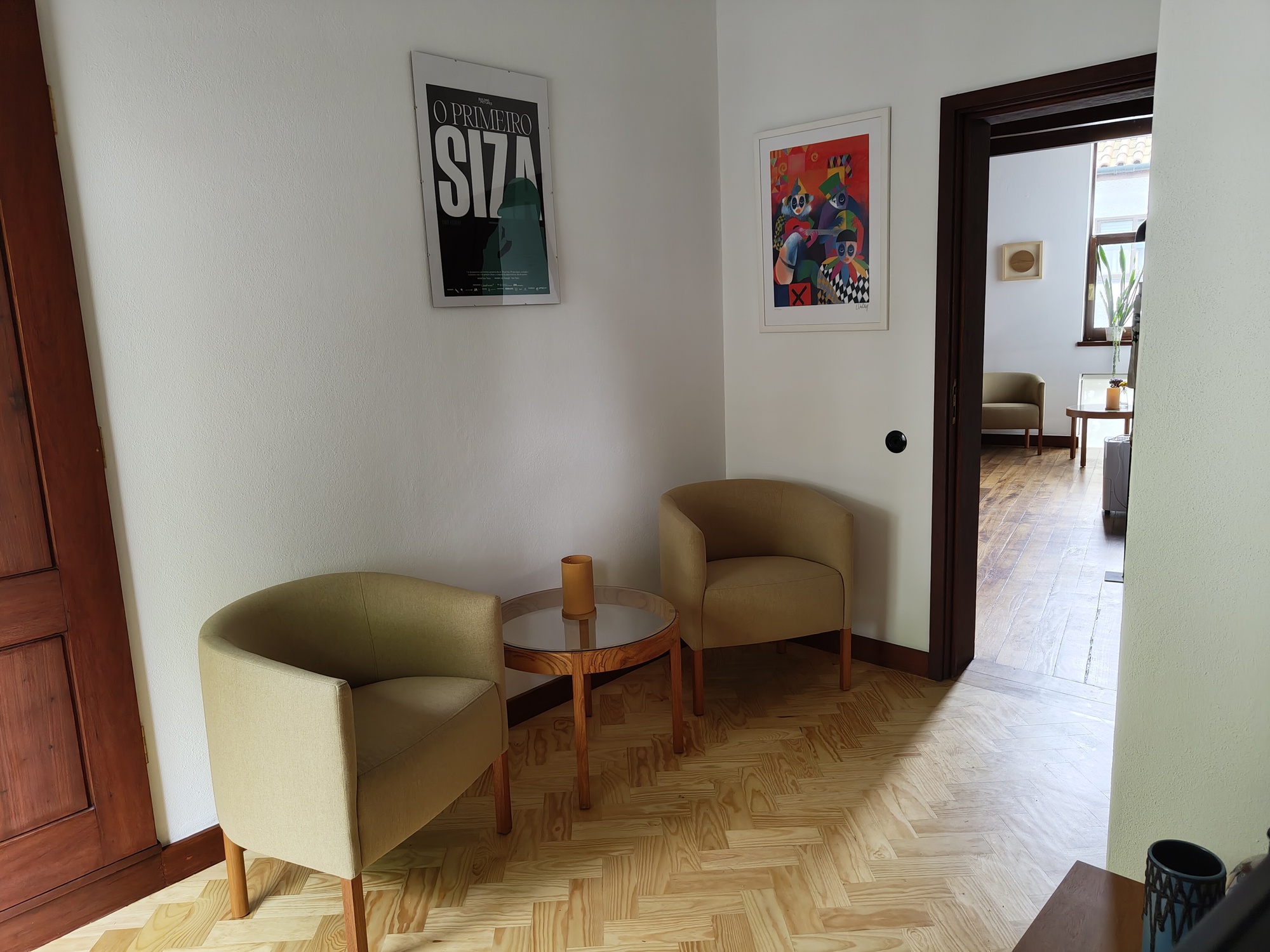 Corridor with herringbone parquet flooring and two upholstered chairs framing a view through a doorway