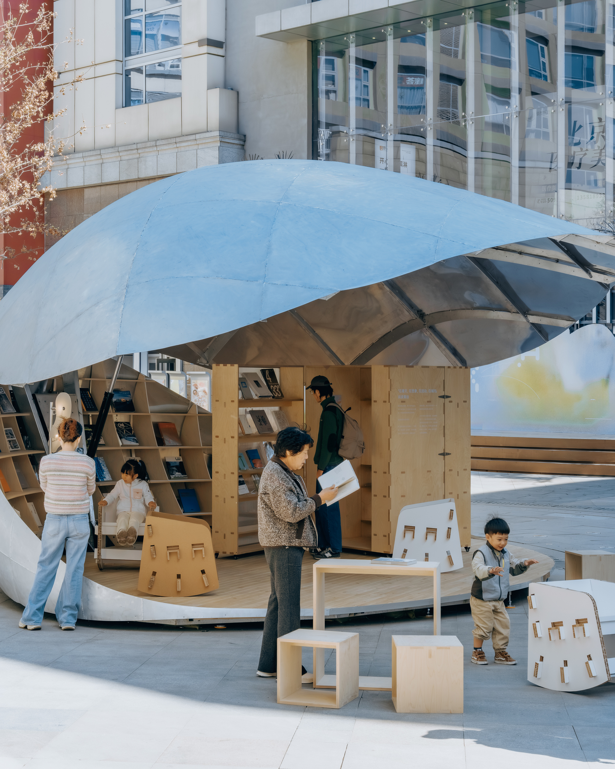 Curved pavilion interior with plywood shelving and furniture occupied by families in afternoon sunlight