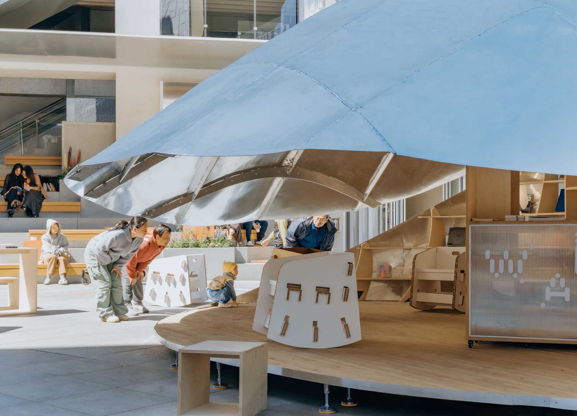 White shell canopy supported by exposed metal ribs above a timber play deck with children and families