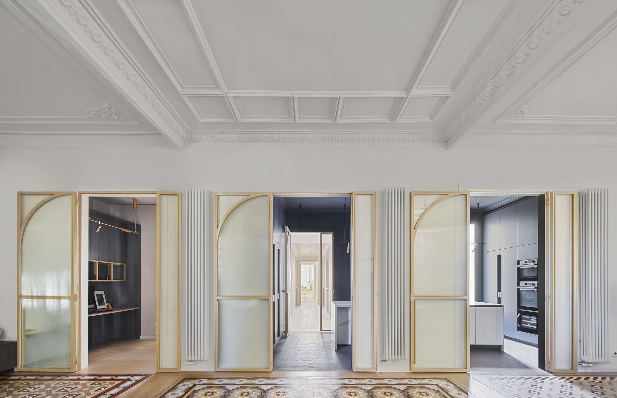 Three brass-framed glass doors with arched tops open from a coffered ceiling room to adjacent spaces
