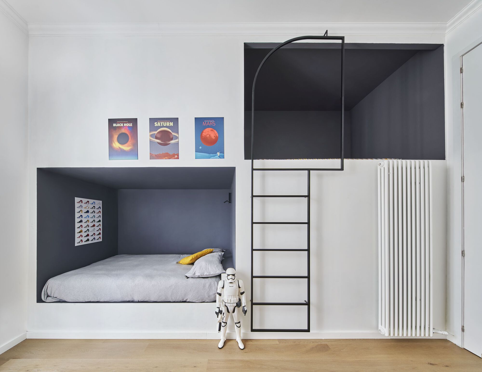 Built-in bunk bed with black steel ladder and storage beside white radiator and space-themed posters