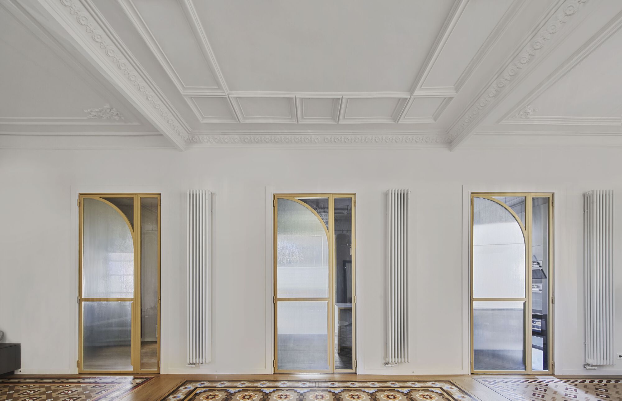 Three brass-framed arched doorways with vertical radiators between them beneath a coffered ceiling