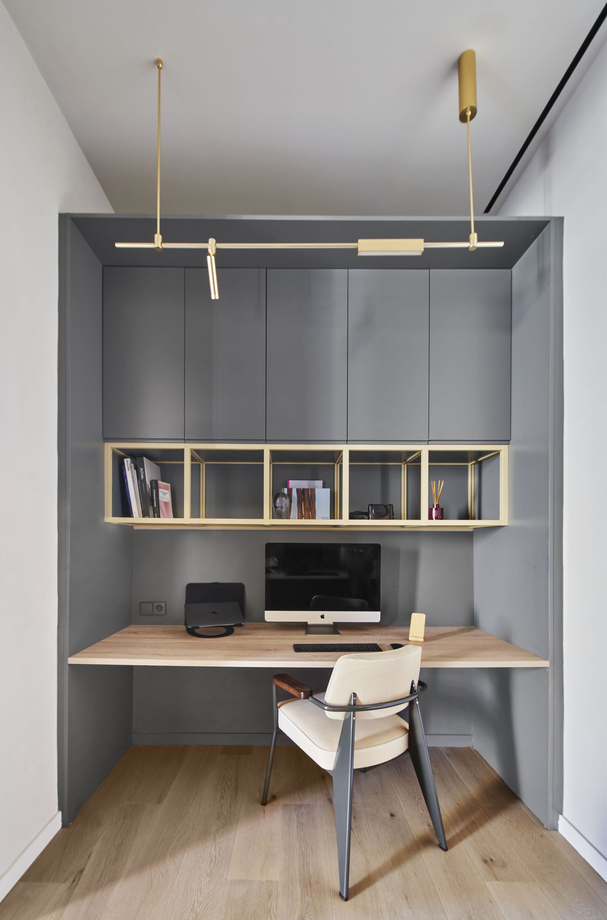 Built-in workspace alcove with grey cabinetry, timber desk, and brass-framed open shelving above
