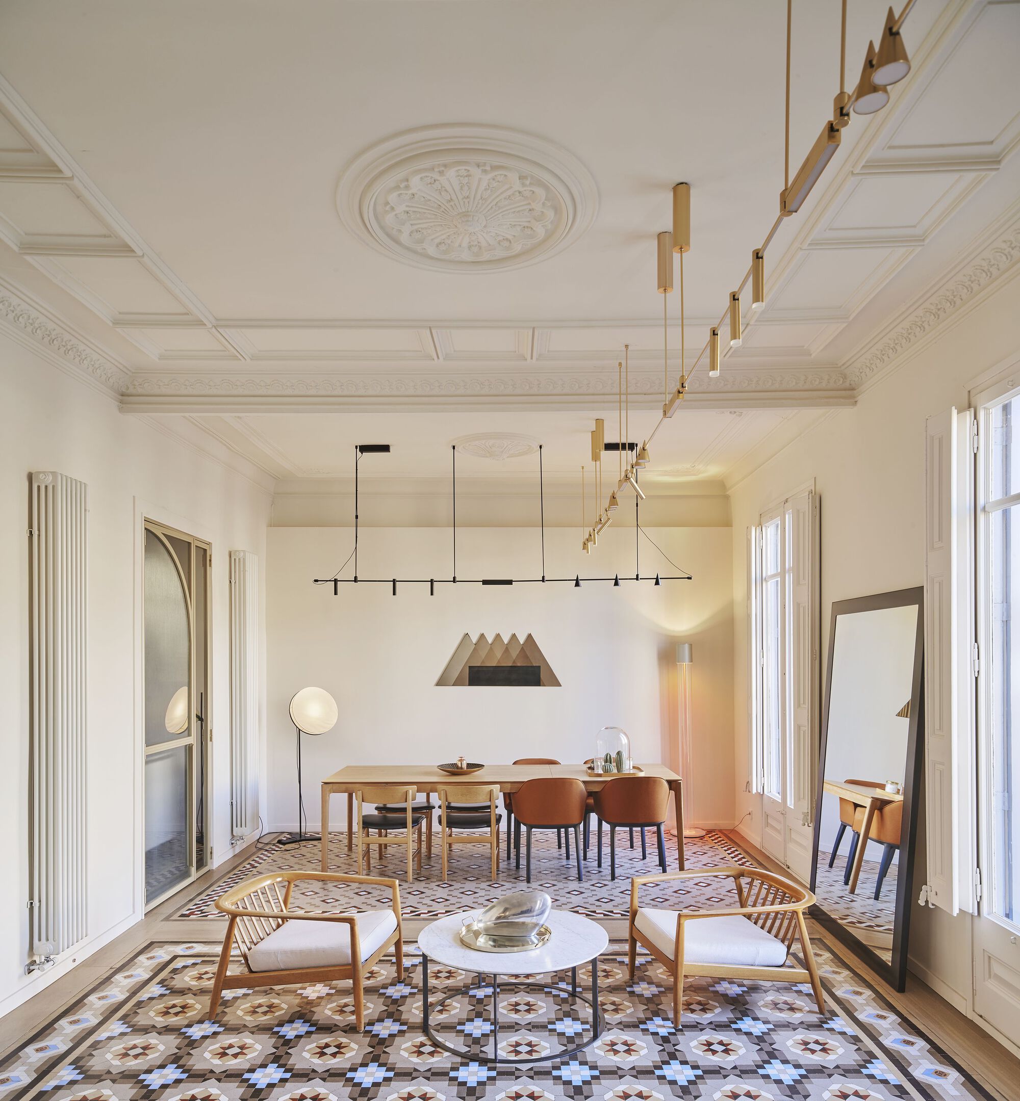 Living and dining area with patterned tile floor, coffered ceiling, and brass chandeliers overhead