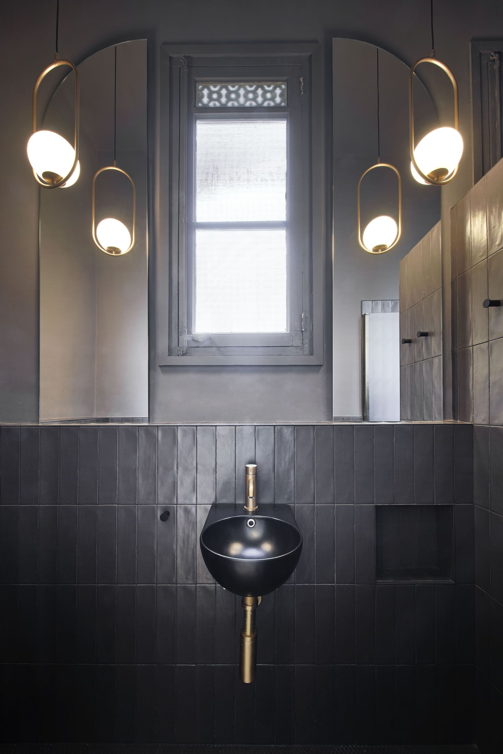 Bathroom vanity with black bowl sink, dark vertical tiles, and paired brass pendant lights