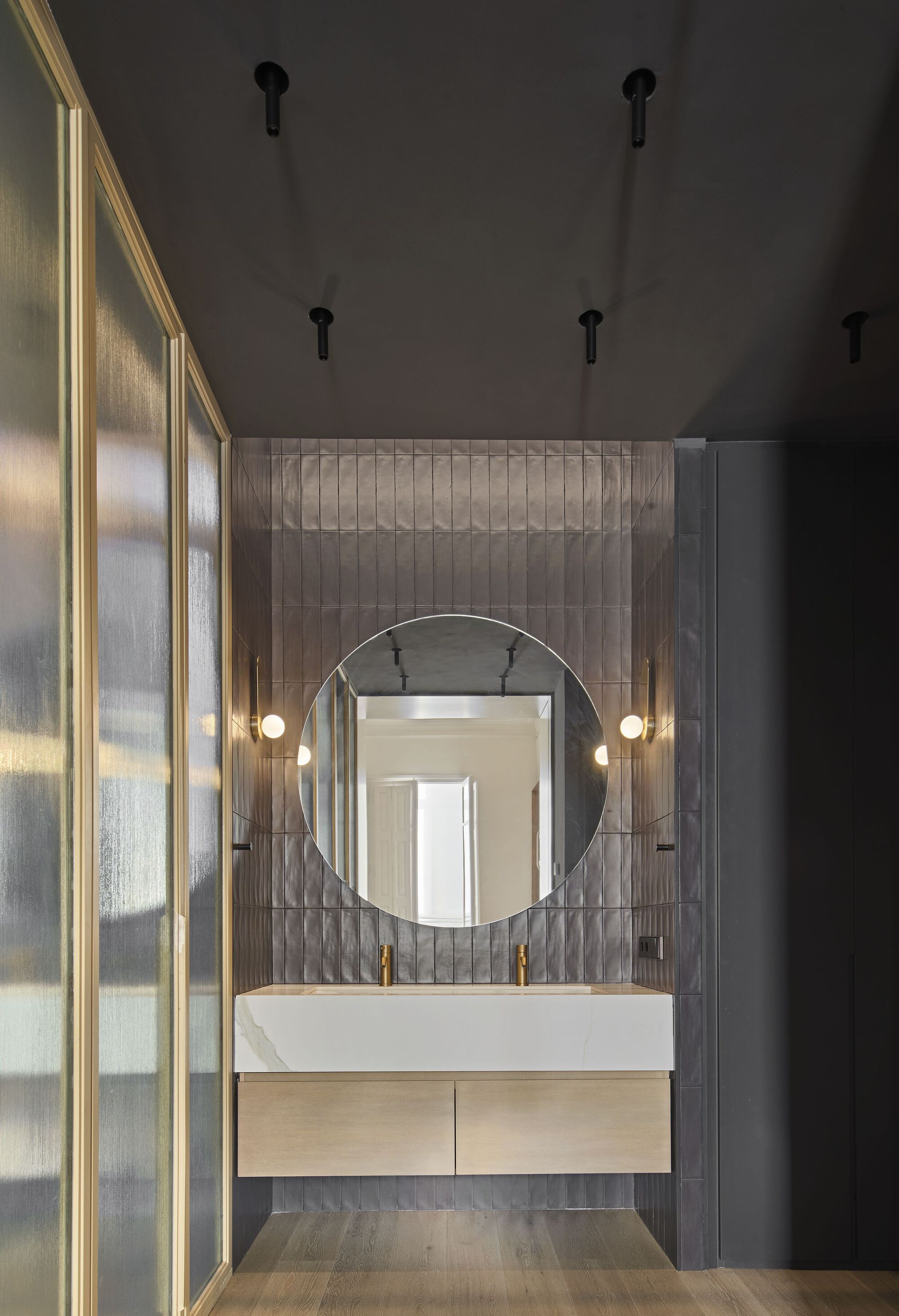 View through the translucent partition into bathroom showing round mirror, floating vanity and symmetrical wall sconces