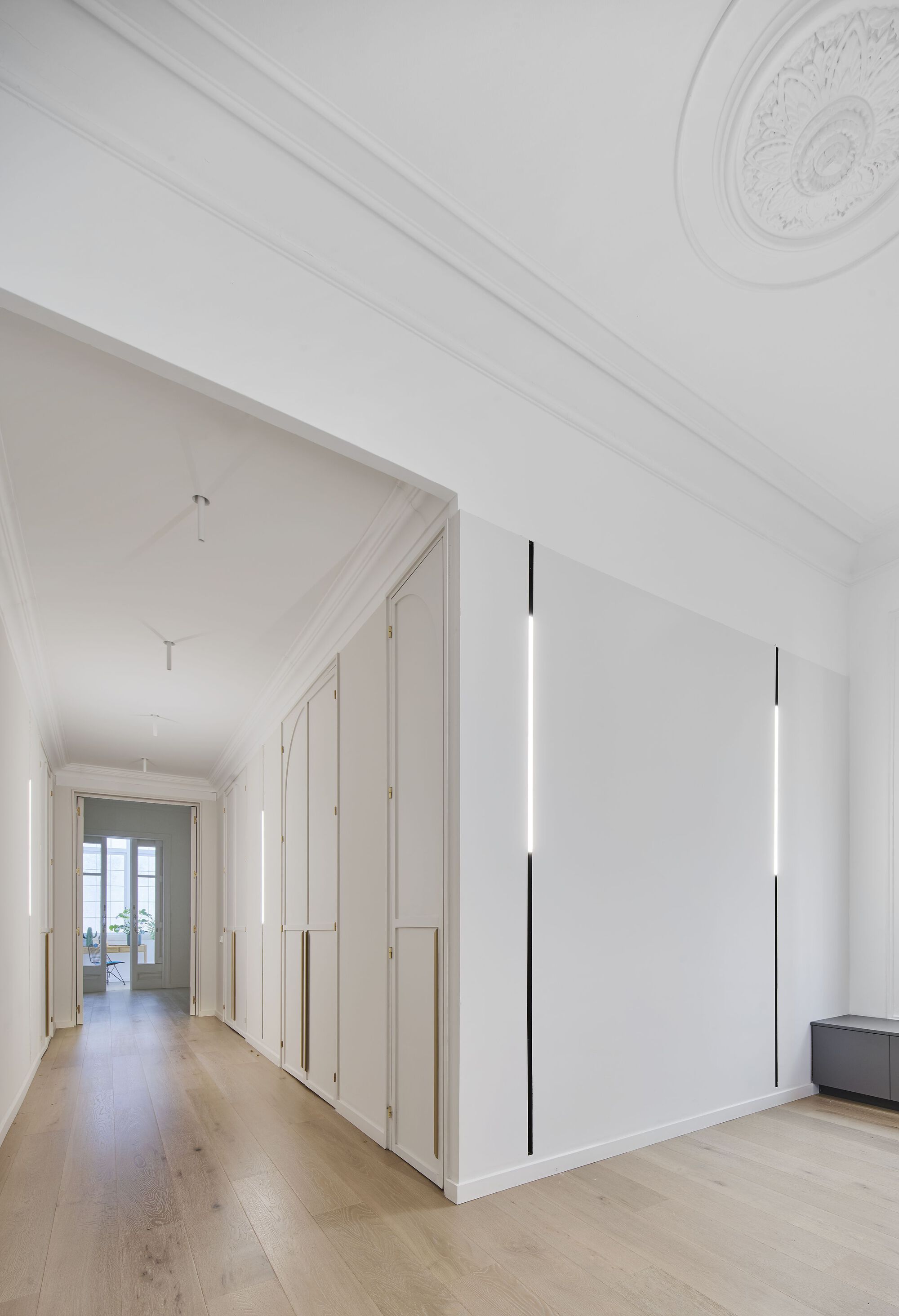 Long hallway with white paneled wardrobes, ceiling rose medallion and vertical black pendant light fixtures