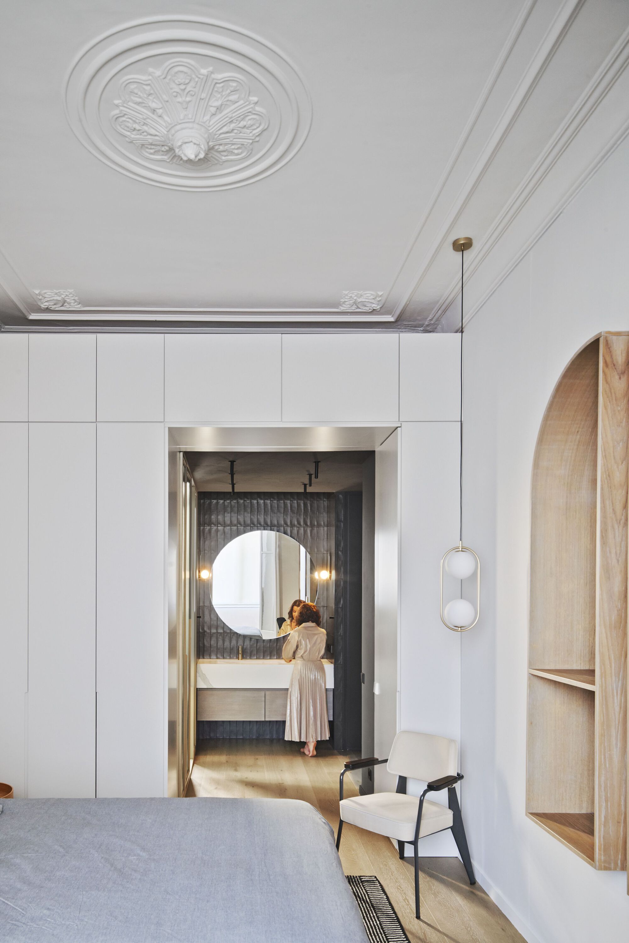Bedroom with ornamental ceiling medallion and view through doorway to ensuite bathroom where figure stands at vanity