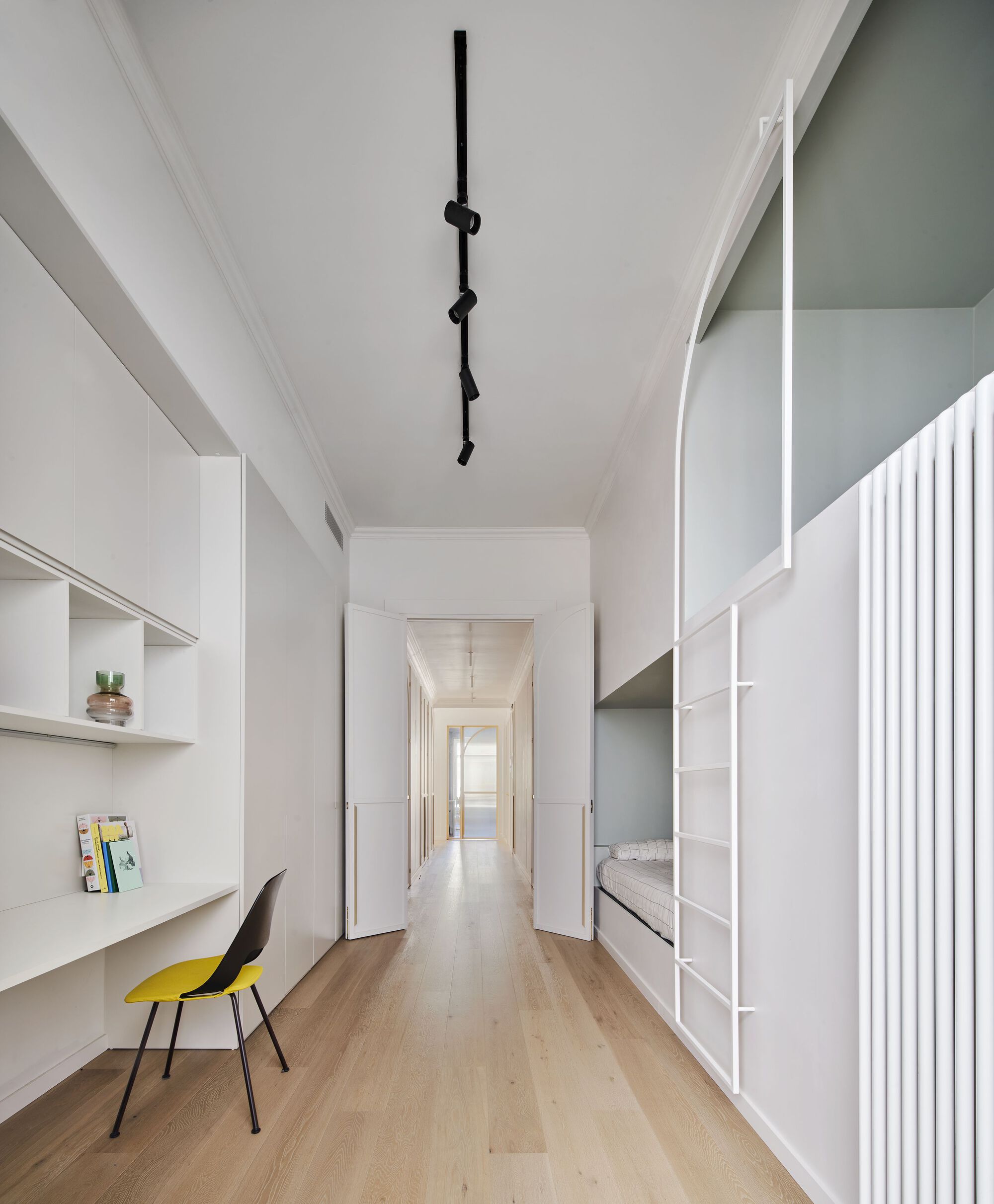 White corridor with built-in desk and storage along both walls under sculptural black ceiling light fixture