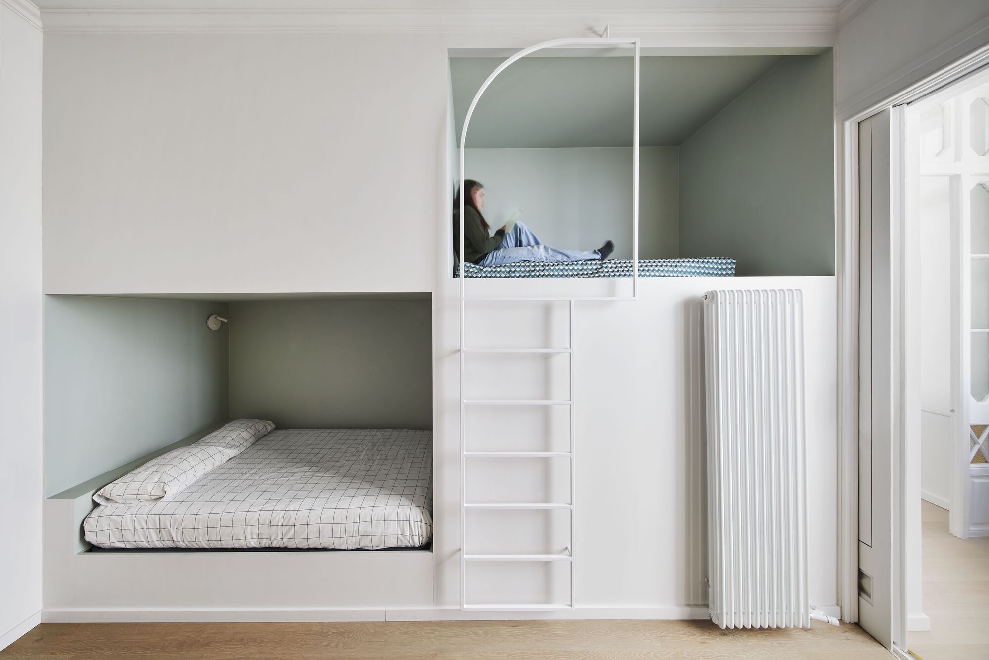 White bunk bed unit with arched upper alcove and ladder access with person reading on top bunk