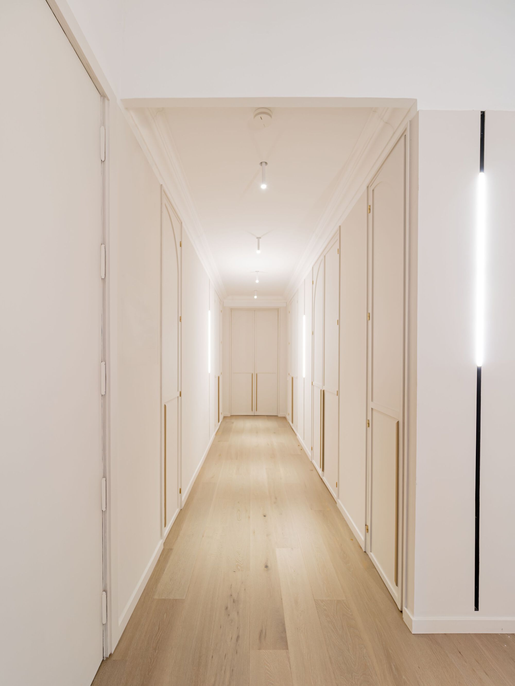 Light wood flooring corridor with flush white paneled doors and recessed ceiling lights