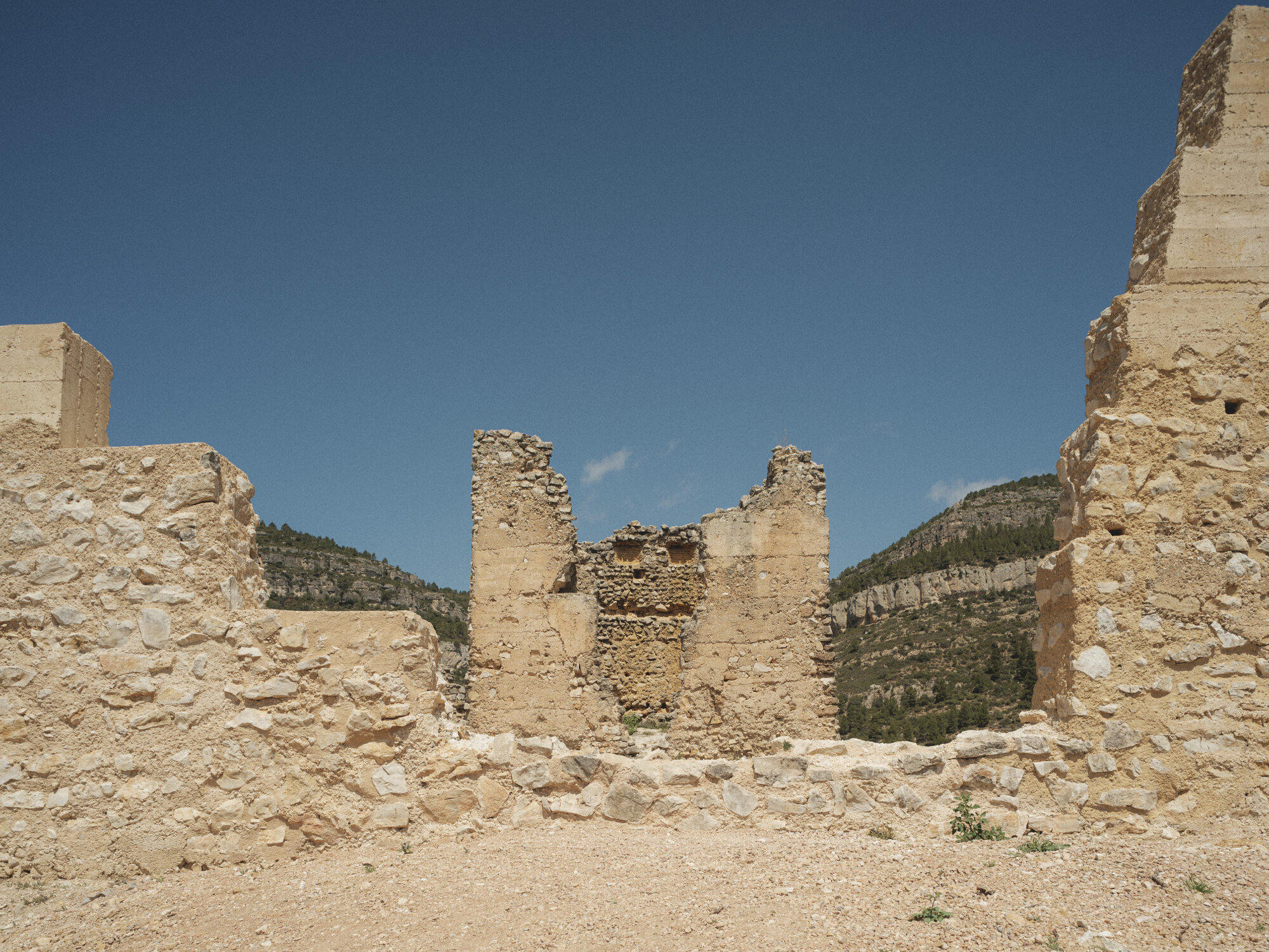 Interior view of ruined stone walls with exposed masonry against a clear blue sky and distant hills