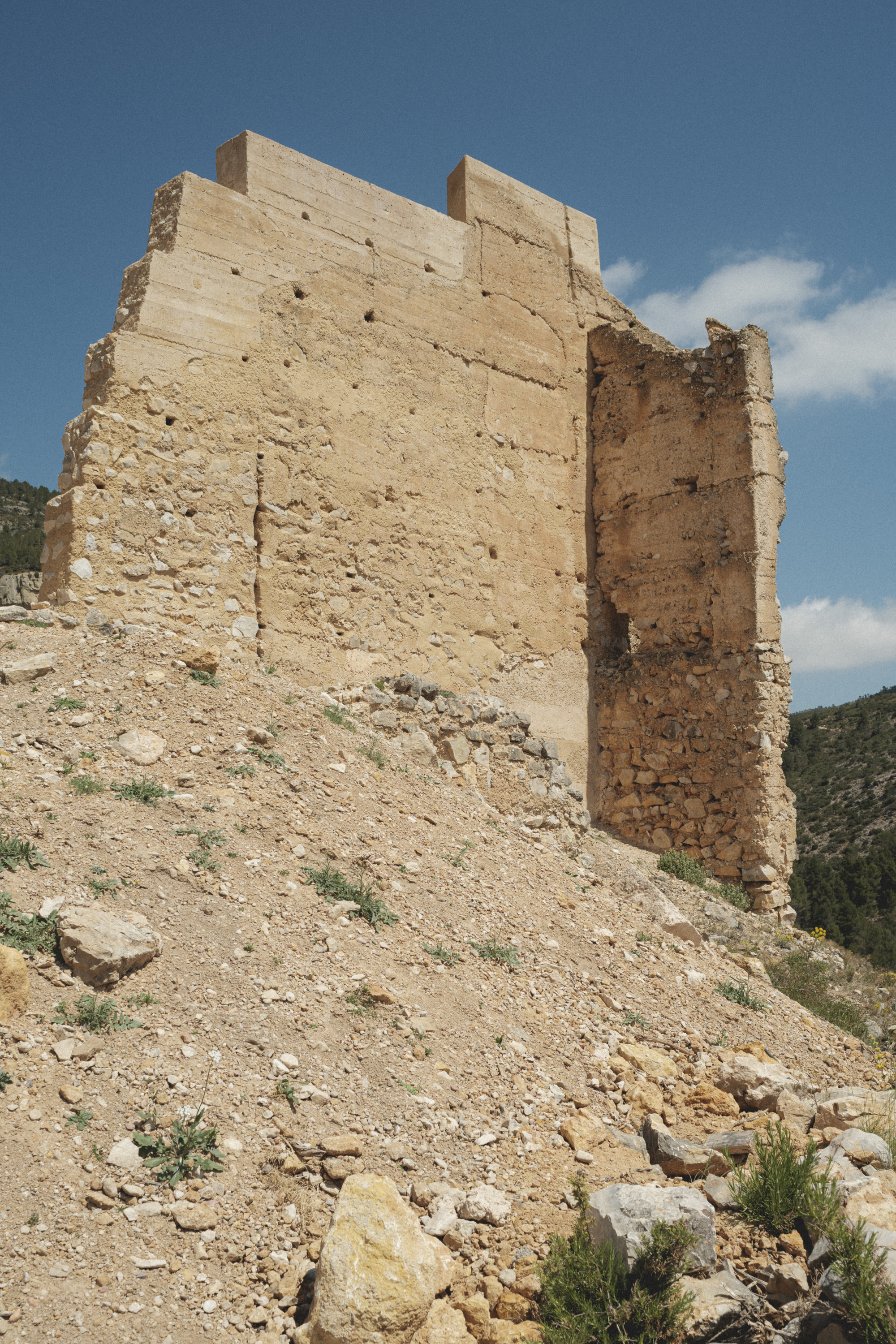 Close view of reconstructed tower wall with visible beam pockets on a steep gravel slope